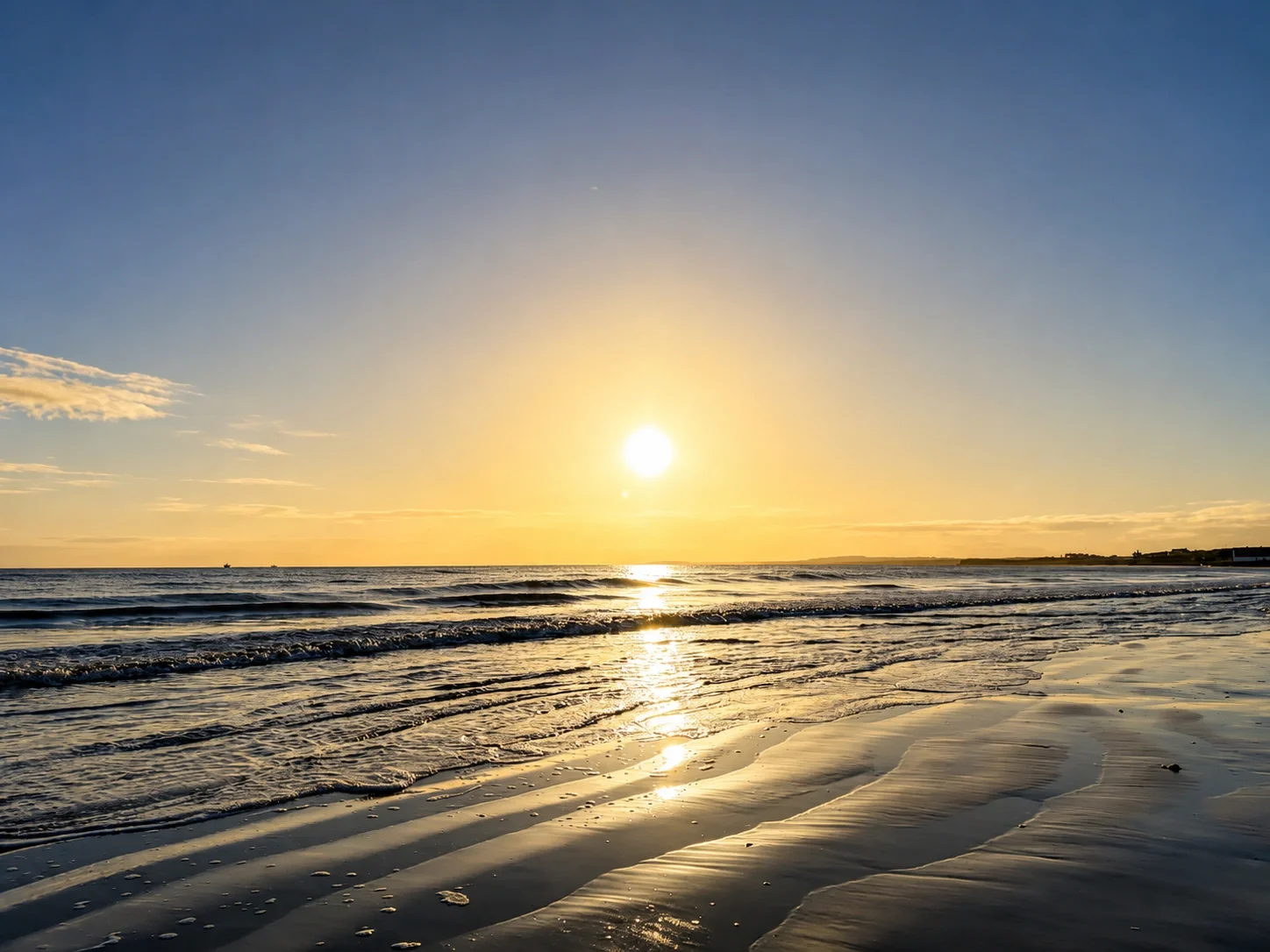Sunset over Dublin Bay with waves gently lapping the sandy beach, reflecting the golden light of the sunset in American English.