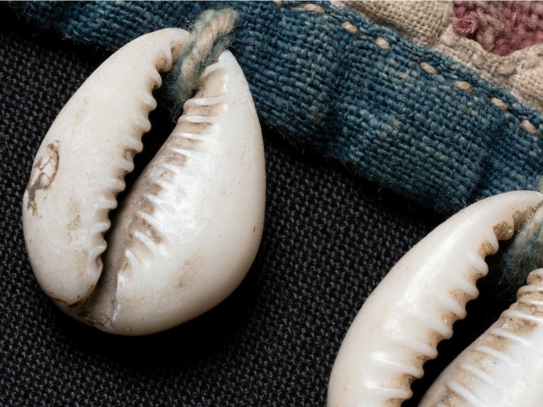 Close-up of three white seashells on dark fabric with a piece of frayed denim and woven cloth in the background.