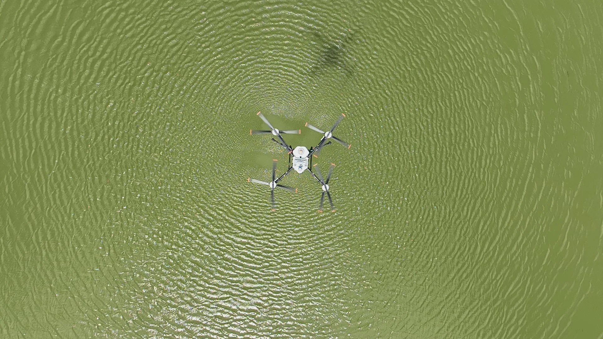 An aerial view of a drone flying over a body of water, creating ripples in the water.