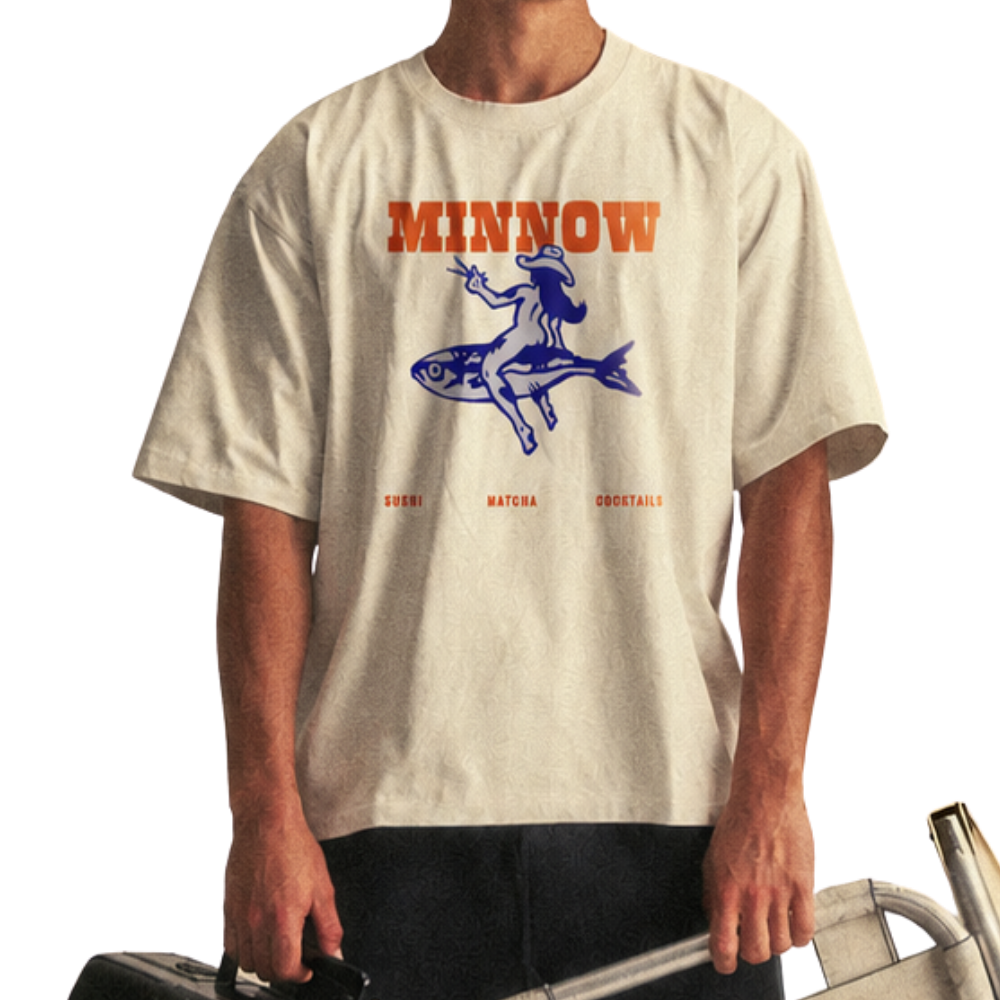 A person wearing a cream-colored t-shirt with the text 'MINNOW' in bold orange letters, a blue graphic of a woman with a hat riding a fish, and smaller text reading 'SUSHI,' 'MATCHA,' and 'COCKTAILS'.