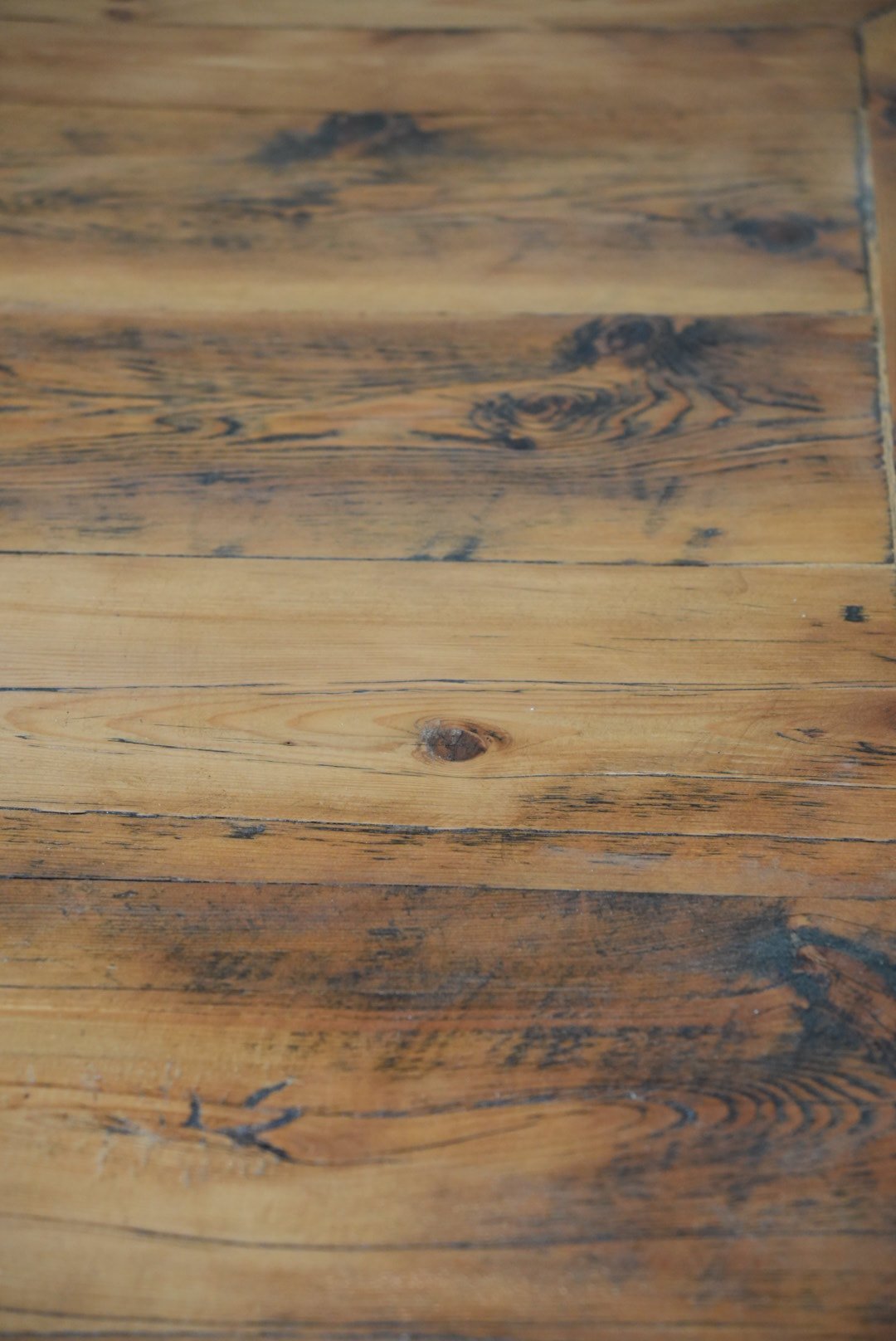Close-up of wooden floorboards showing natural wood grain, knots, and some dark stains.