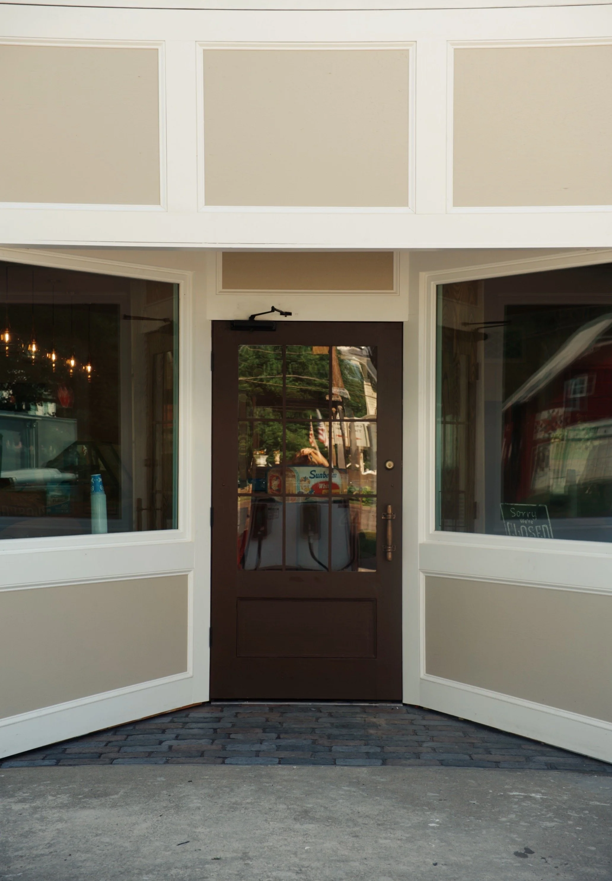 Front of a storefront with a black door, large glass windows on either side, white trim, and a sign in the window that reads "Sorry we're CLOSED."