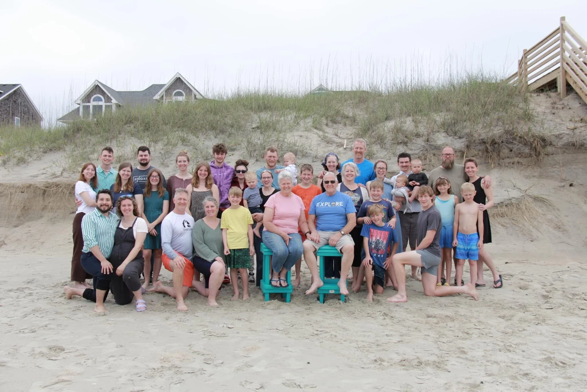 Group of people on a beach, smiling for a photo with sand dunes and houses in the background.