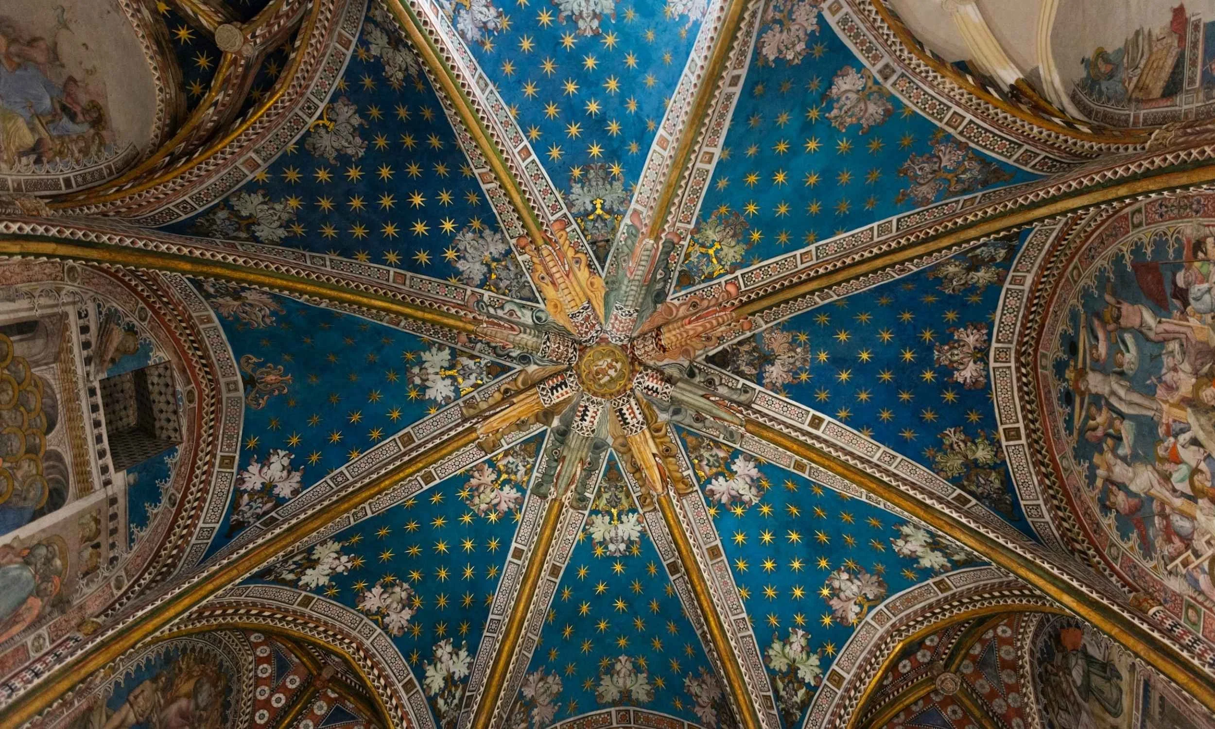 Colorful architectural ceiling with a blue background, gold stars, intricate patterns, and religious or historical murals.