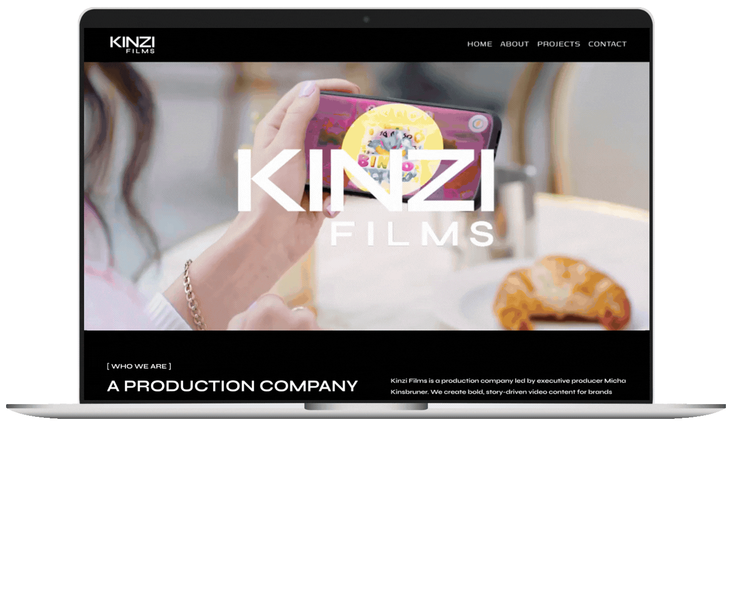 Screenshot of Kinzi Films website on a laptop, showing a person holding a phone with a cartoon image on the screen, some baked goods nearby, and website navigation options at the top.