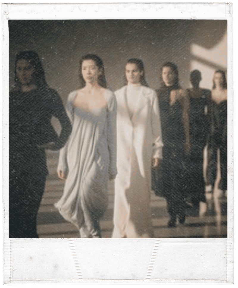 Group of women walking down stairs in elegant attire, with a woman in the front wearing a light-colored gown and the others in darker dresses.