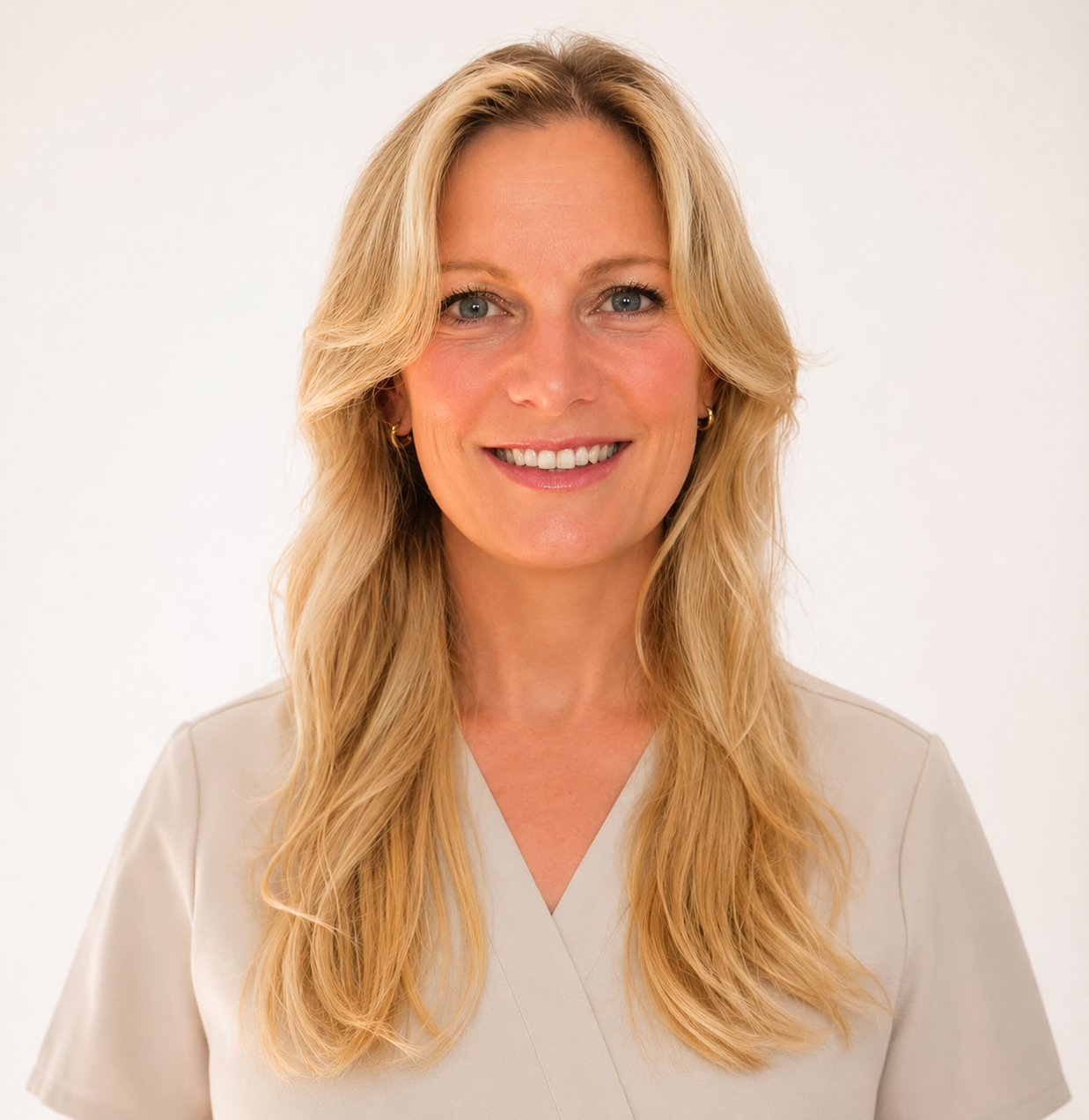A smiling woman with long, wavy blonde hair wearing a light beige top, posing against a plain white background.