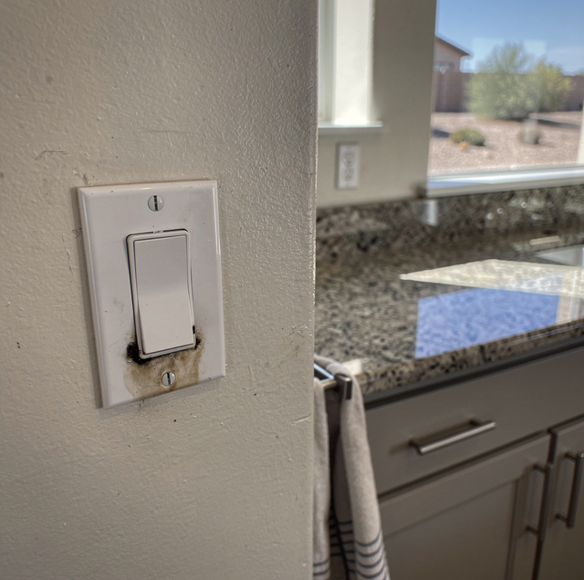 Light switch on textured wall near window with view of countertop and outdoor desert landscape.