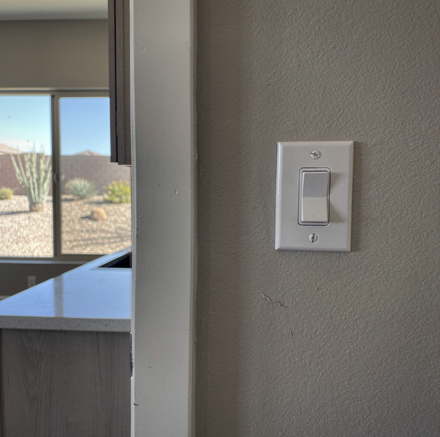 Light switch on textured wall next to window overlooking desert landscape with mountains.