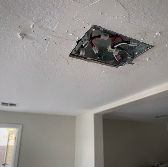 An open electrical box mounted in a drywall ceiling with red, black, and white wires and connectors visible.