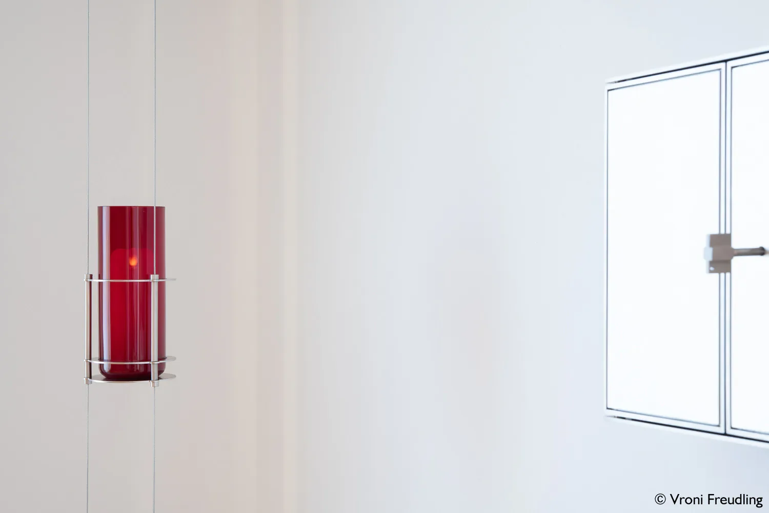 Ein roter Feuerlöscher an einer weißen Wand in einem modernen Raum, rechts eine weiße Schranktür.