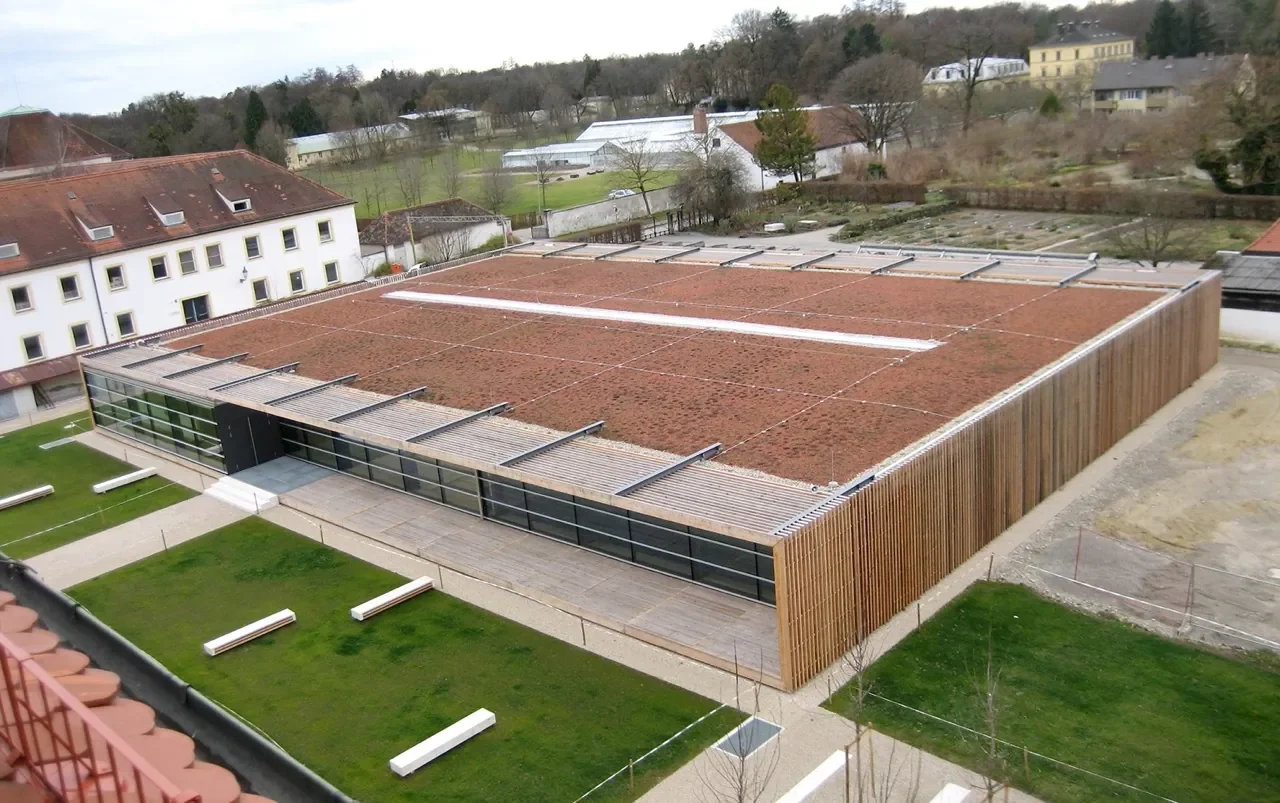 Modernes Gebäude mit großem Flachdach, umgeben von Grünflächen und Bäumen, in einer ruhigen, ländlichen Umgebung.