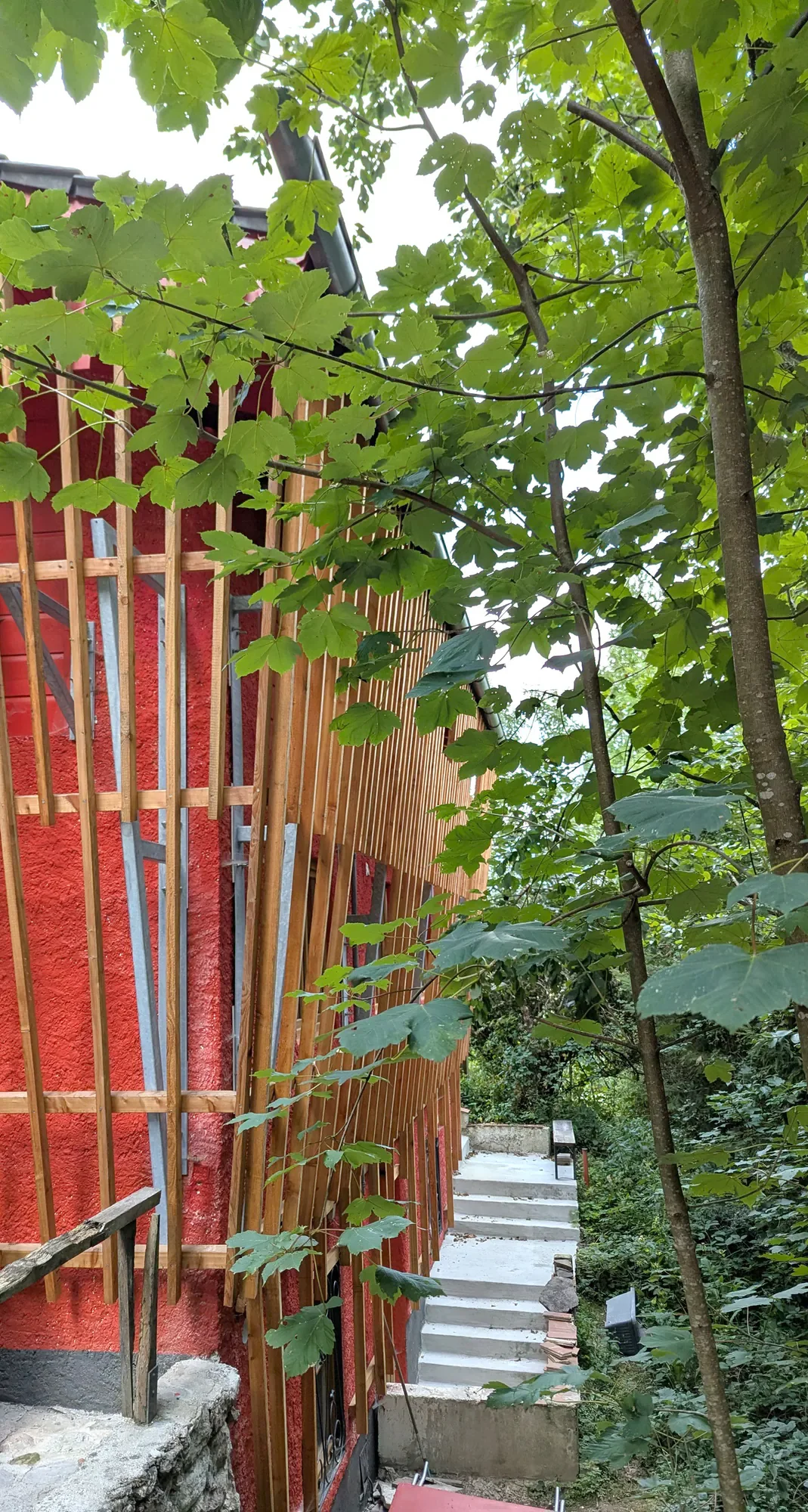 Ein Haus mit roter Wand und Holzrahmen, umgeben von grünen Bäumen, mit einer Treppe im Vordergrund.