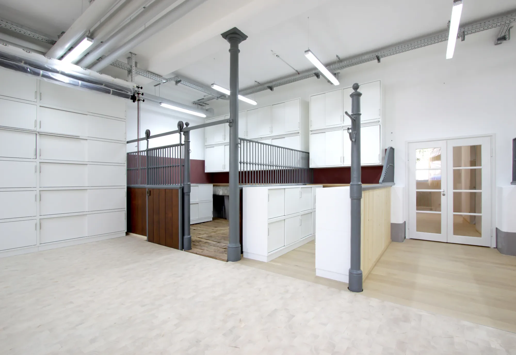 Innenansicht eines Hauses im Bau oder Renovierung, sichtbare Rohre und Gerüste, helle Wände und Boden, nach oben gerichtete Beleuchtung.