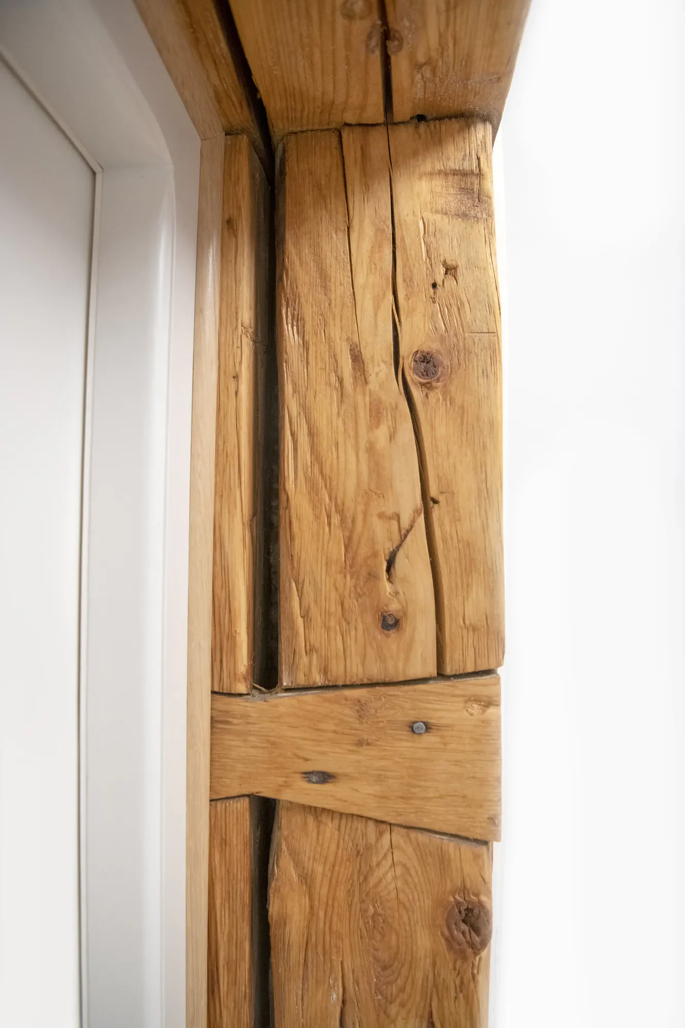 Holzleisten und Holzstämme an einer Wand, sichtbare Risse und Maserung, teilweise mit Schrauben befestigt.