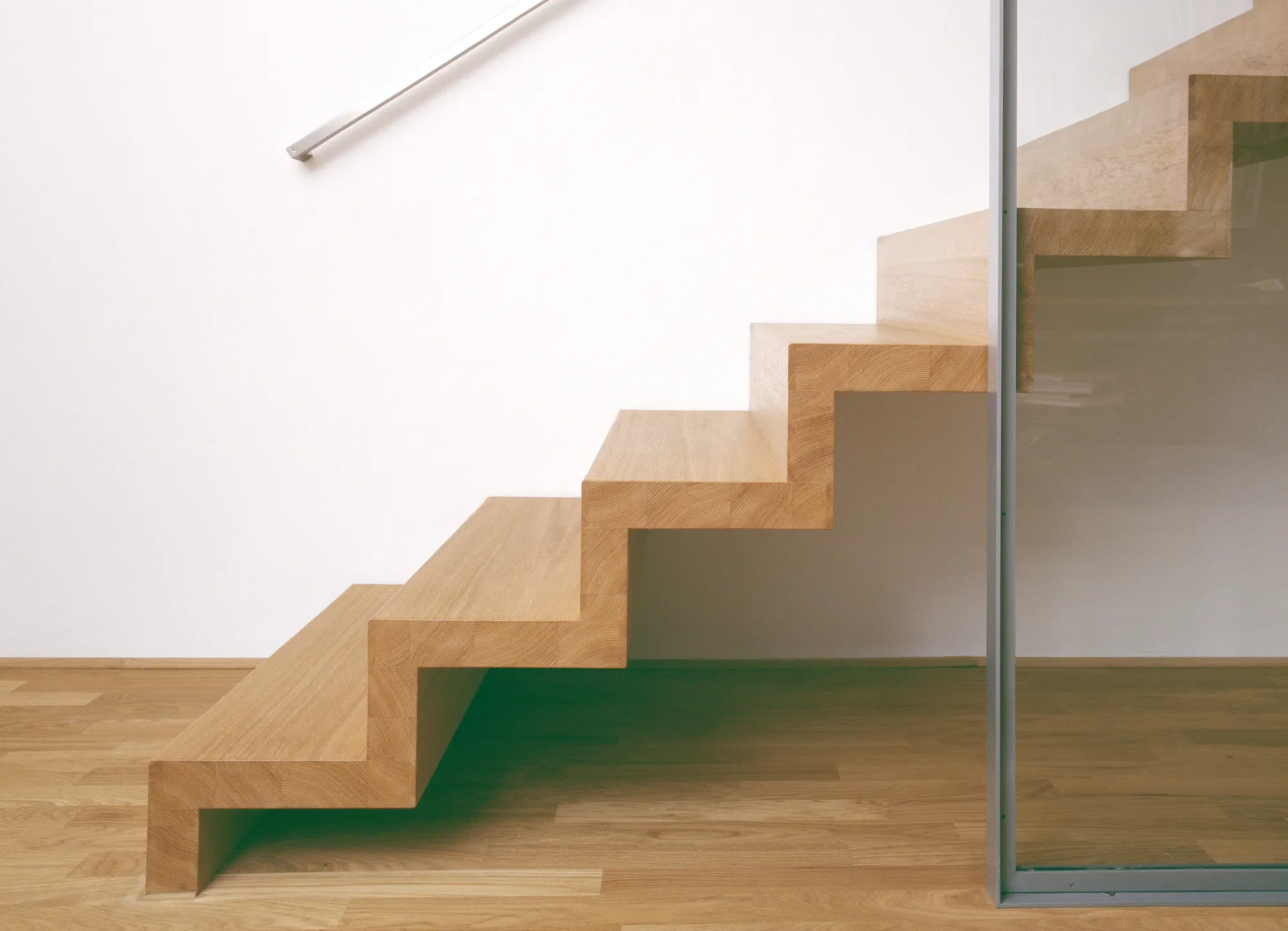 Holztreppe mit Glasgeländer in einem modernen Gebäude.