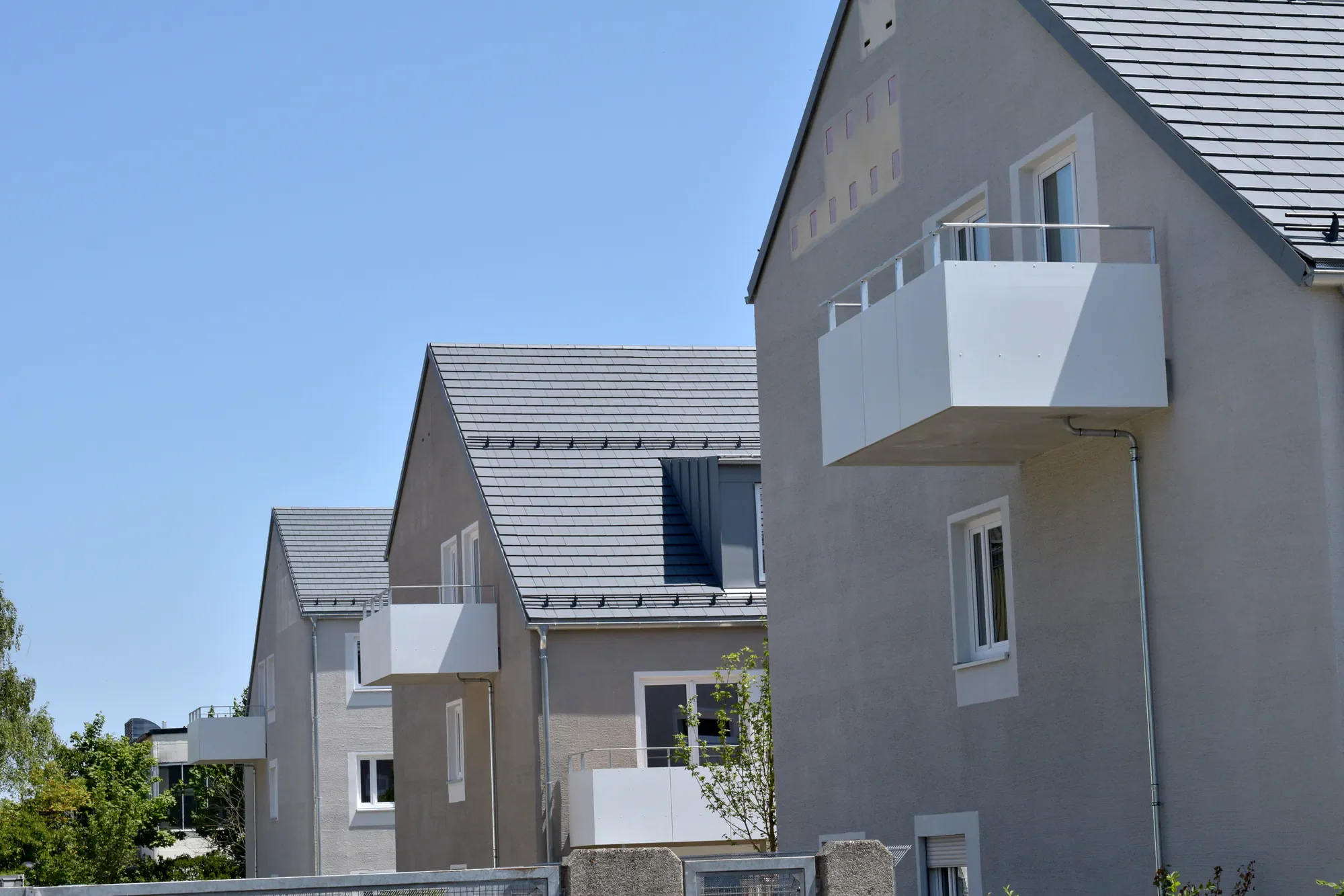 Mehrstöckiges modernes Wohngebäude mit weißen Wänden, Balkonen und großen Fenstern, unter einem blauen Himmel