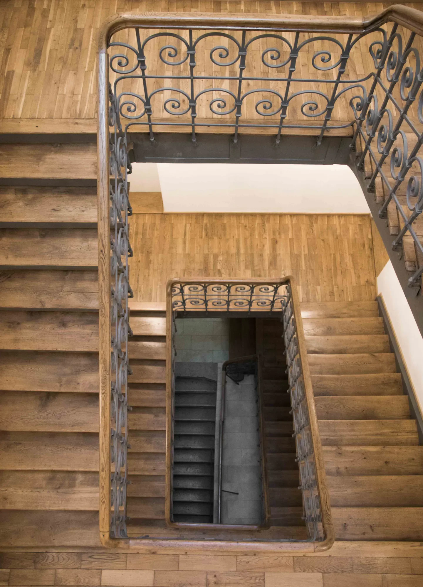 Blick von oben auf eine Holztreppe mit verzierter Eisenbalustrade, die nach unten führt, auf Holzfußboden.