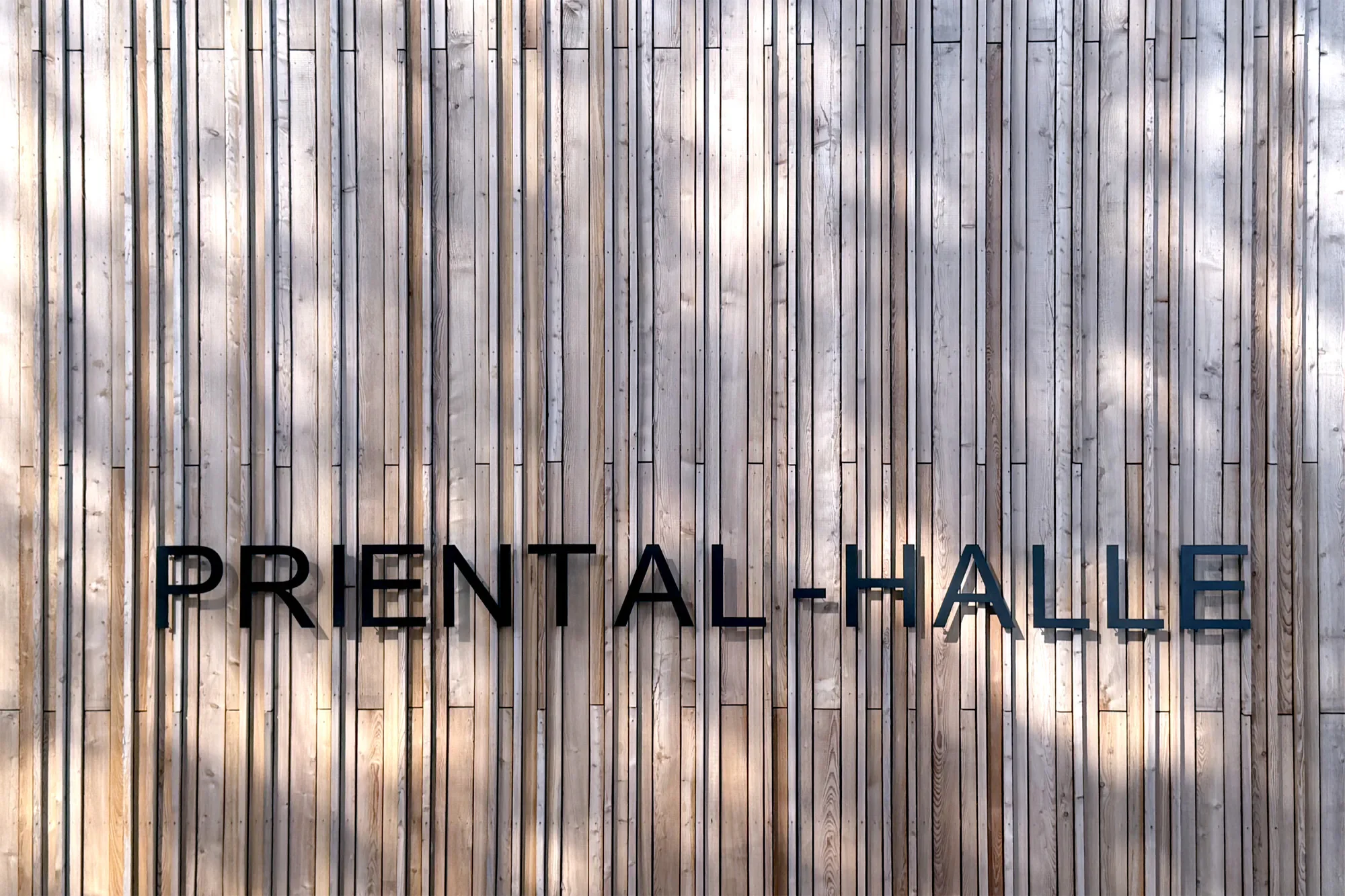 Holzwand mit dem Schriftzug 'PRESENT AL-HALLE'