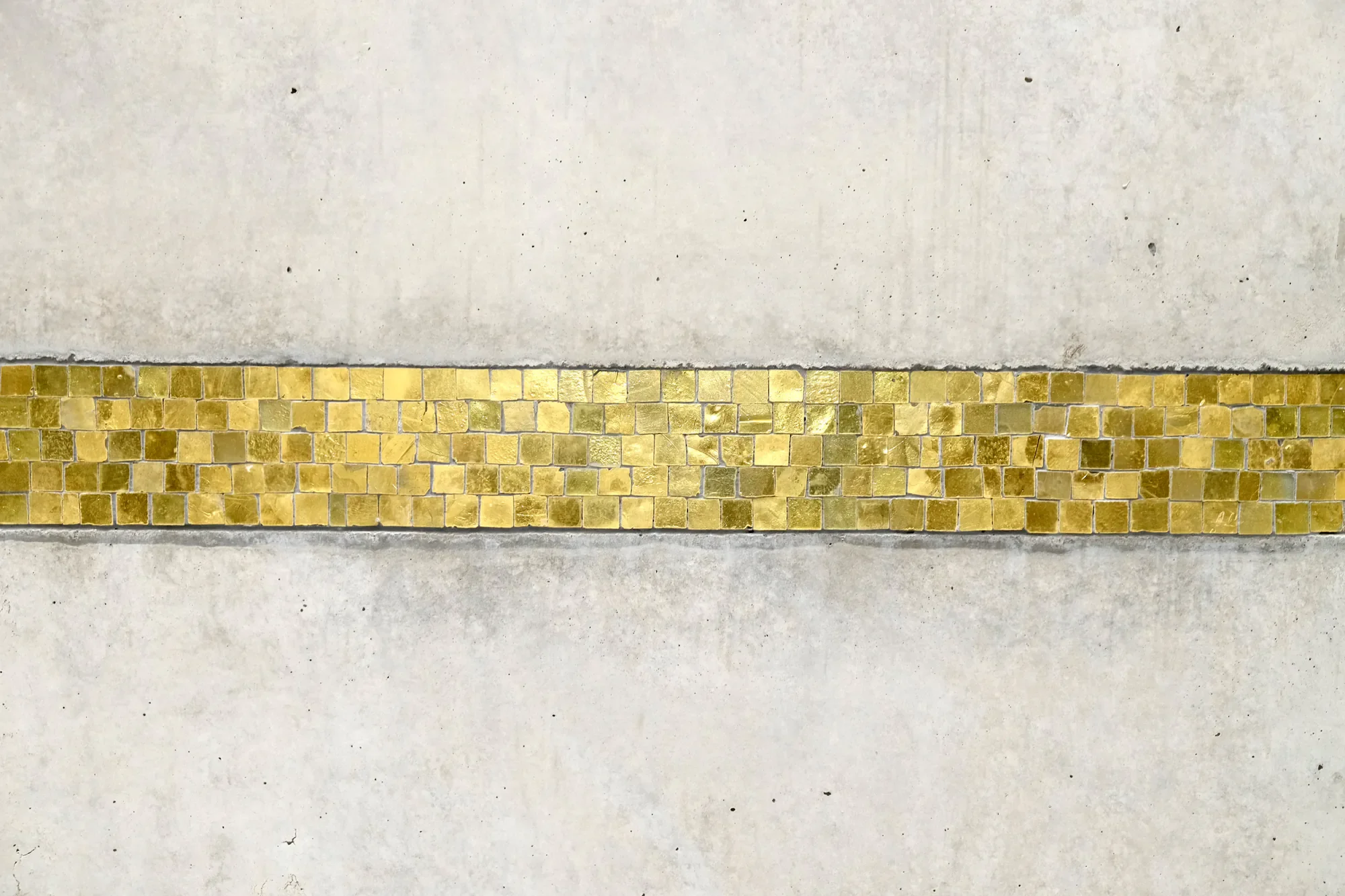 Eine weiße Wand mit einer dünnen goldfarbenen Mosaiklinie am unteren Rand.