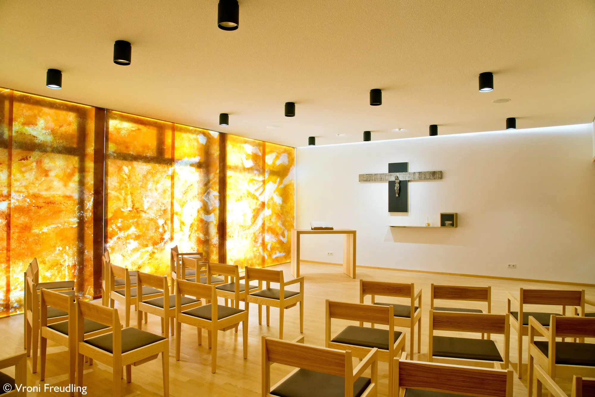 Ein leeres Kirchenraum mit Stühlen, goldener Altarglasur und einem Kreuz an der Wand.