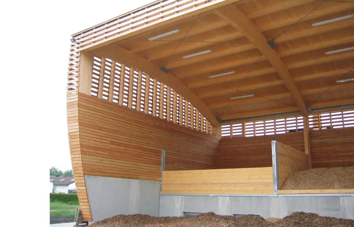 Ein Gebäude aus Holz mit einem offen einsehbaren oberen Bereich in einer landwirtschaftlichen Umgebung, vermutlich eine Scheune oder Stall.