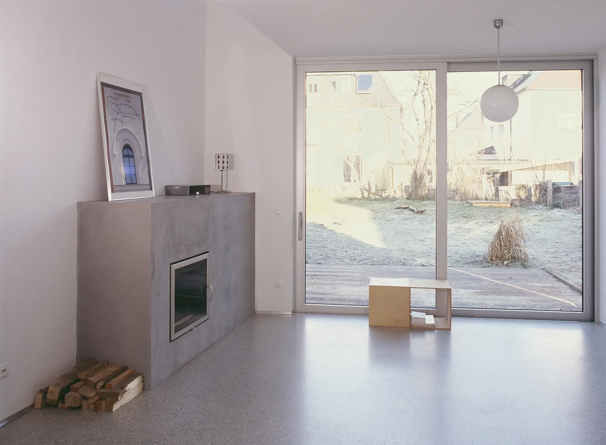Innenraum eines modernen Hauses mit großen Glastüren, Blick nach draußen auf einen Garten, minimalistischer Stil, Lampe an der Decke.