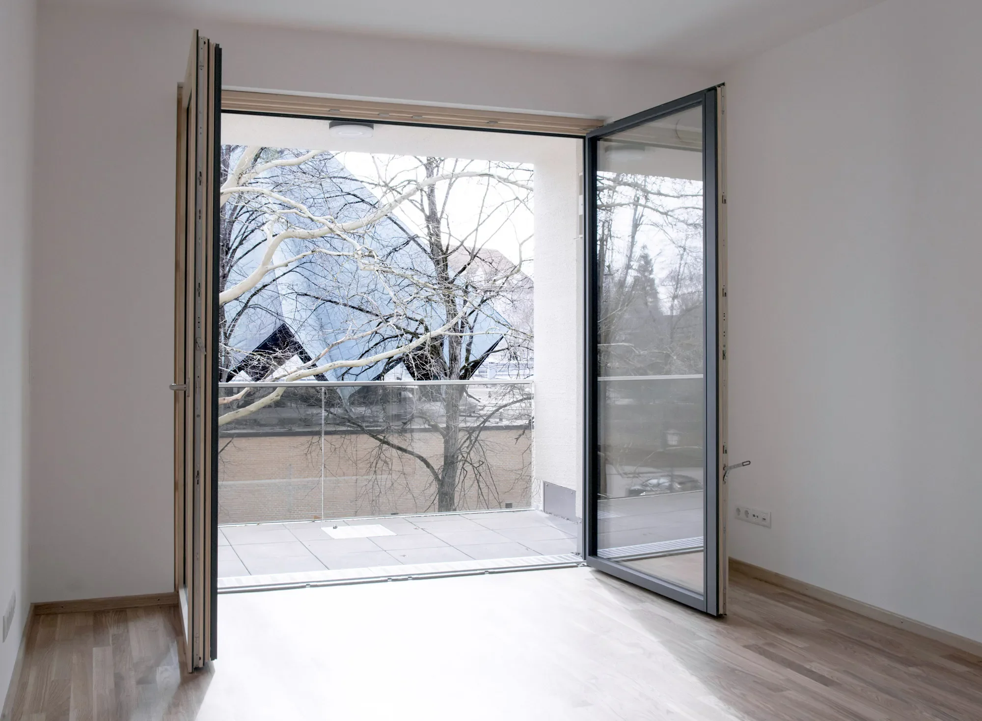 Leeres, modern eingerichtetes Zimmer mit französischem Balkon und Blick auf verschneite Bäume draußen.