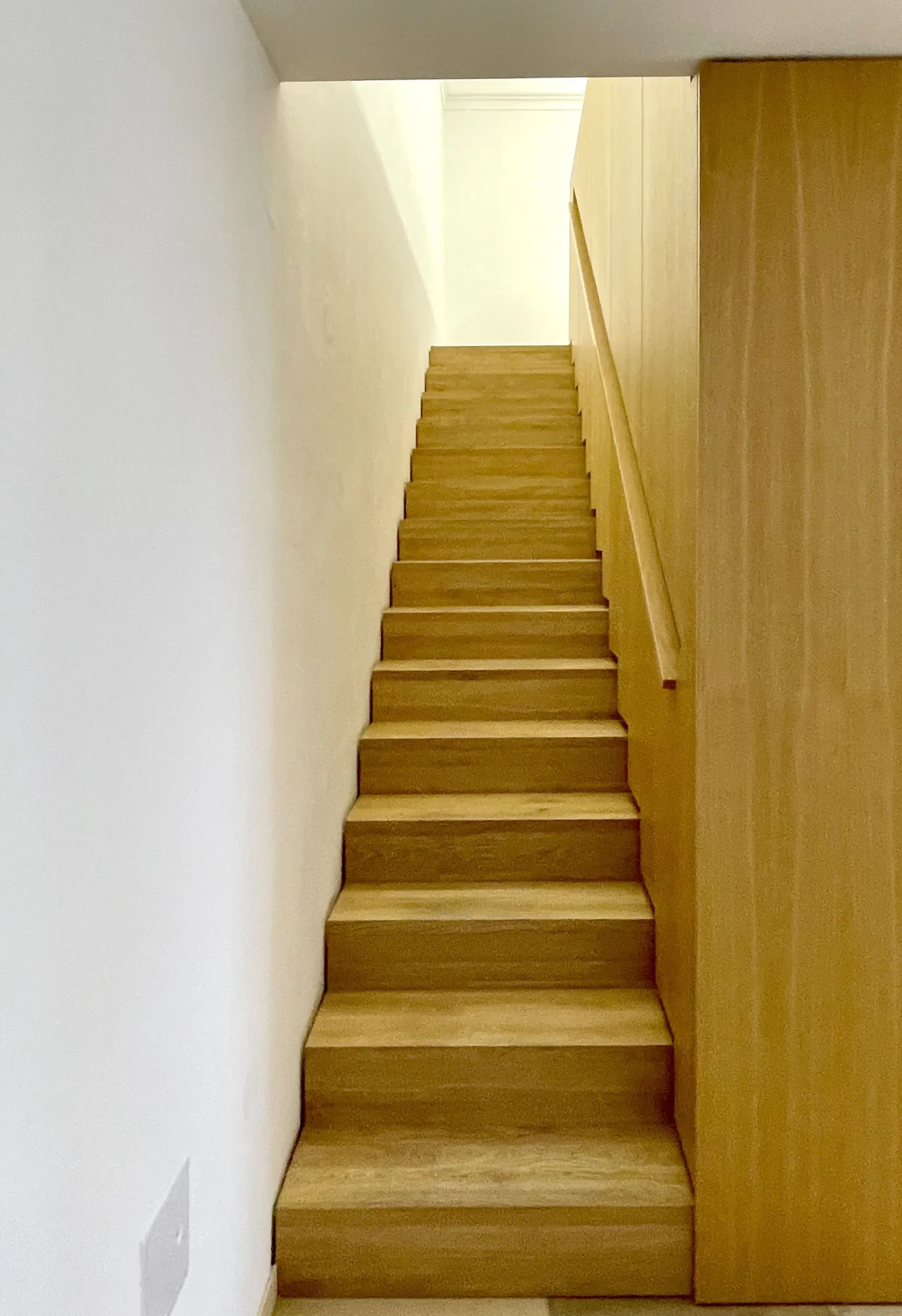 Ein Holzregal oder eine Holzkonsole, die entlang einer weißen Wand platziert ist, im Innenraum eines Hauses oder einer Wohnung, mit einem unteren Boden aus Holz.