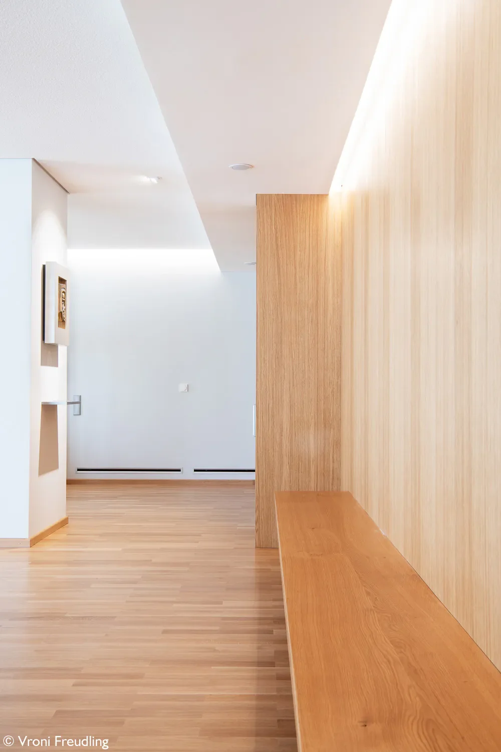 Innenraum mit Holzbank und Wand, klarer moderner Stil, helles Licht.