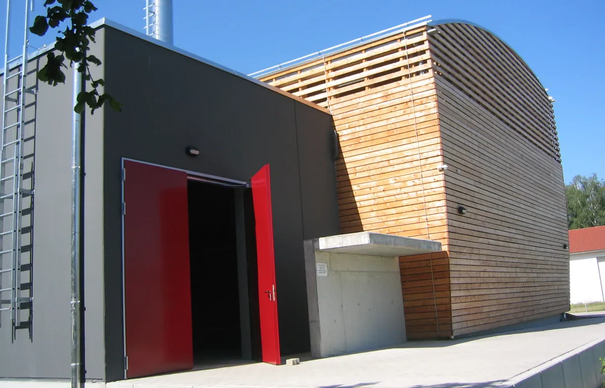 Moderne Gebäude mit Holz- und dunklen Fassaden, roter Eingangstür und blauer Himmel.