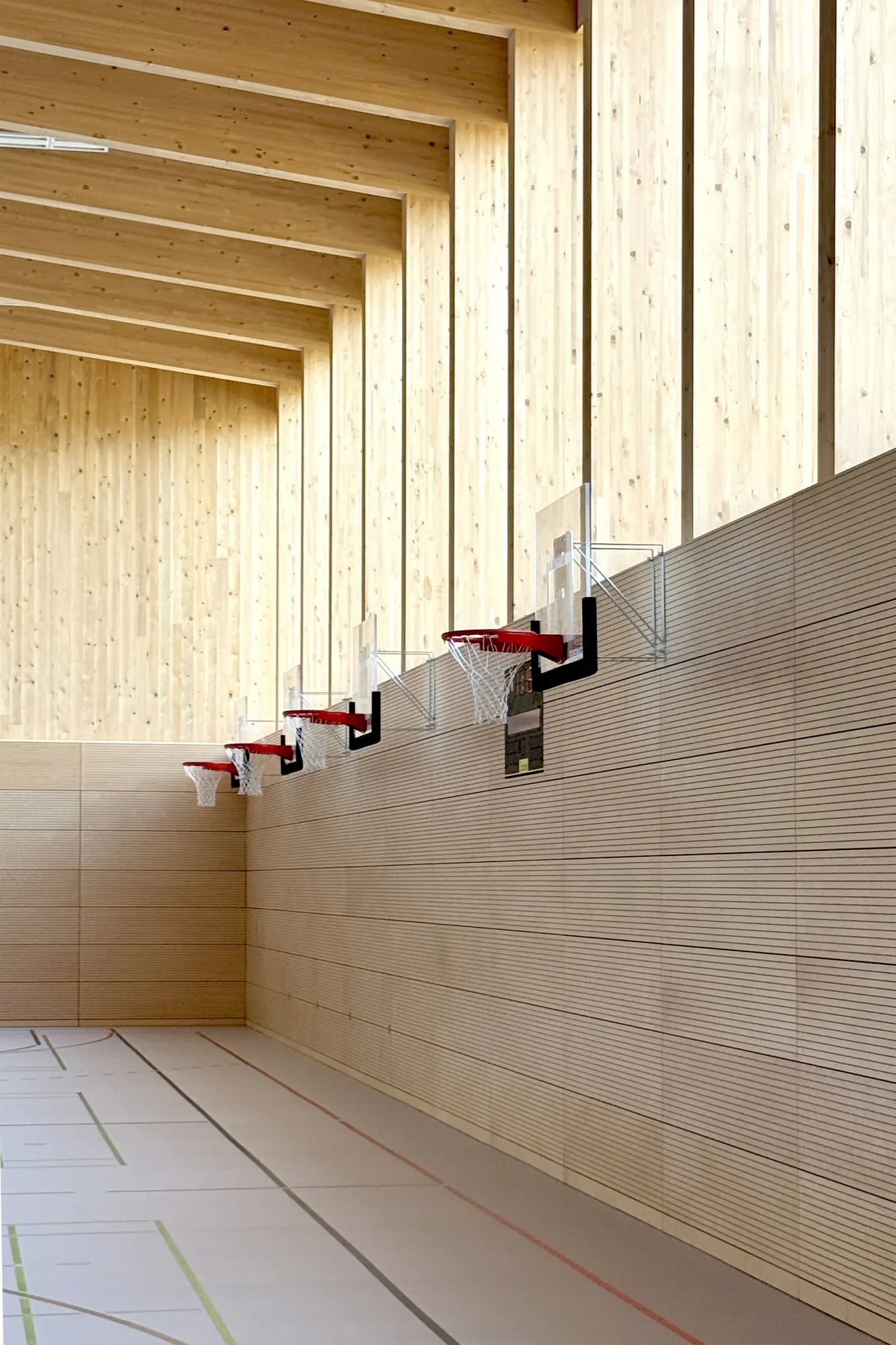 Innensicht eines Turnhallenbodens mit mehreren Basketballkörben an der Wand. Die Wände sind mit Holz verkleidet und der Boden hat Markierungen für verschiedene Sportarten.