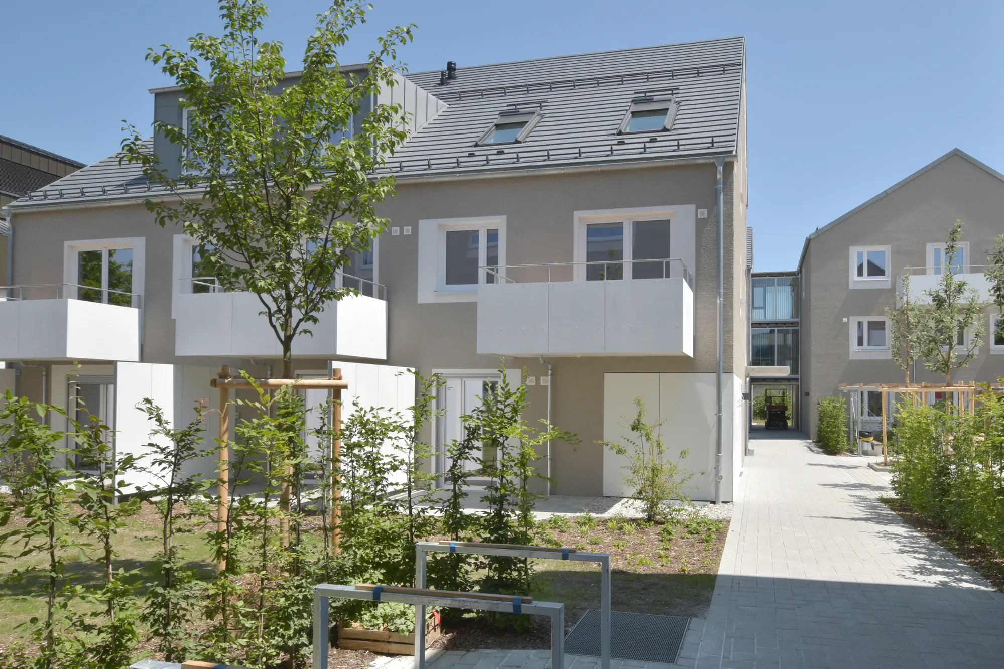 Moderner Wohnkomplex mit Balkon, Dachfenstern und grüner Umgebung bei schönem Wetter.