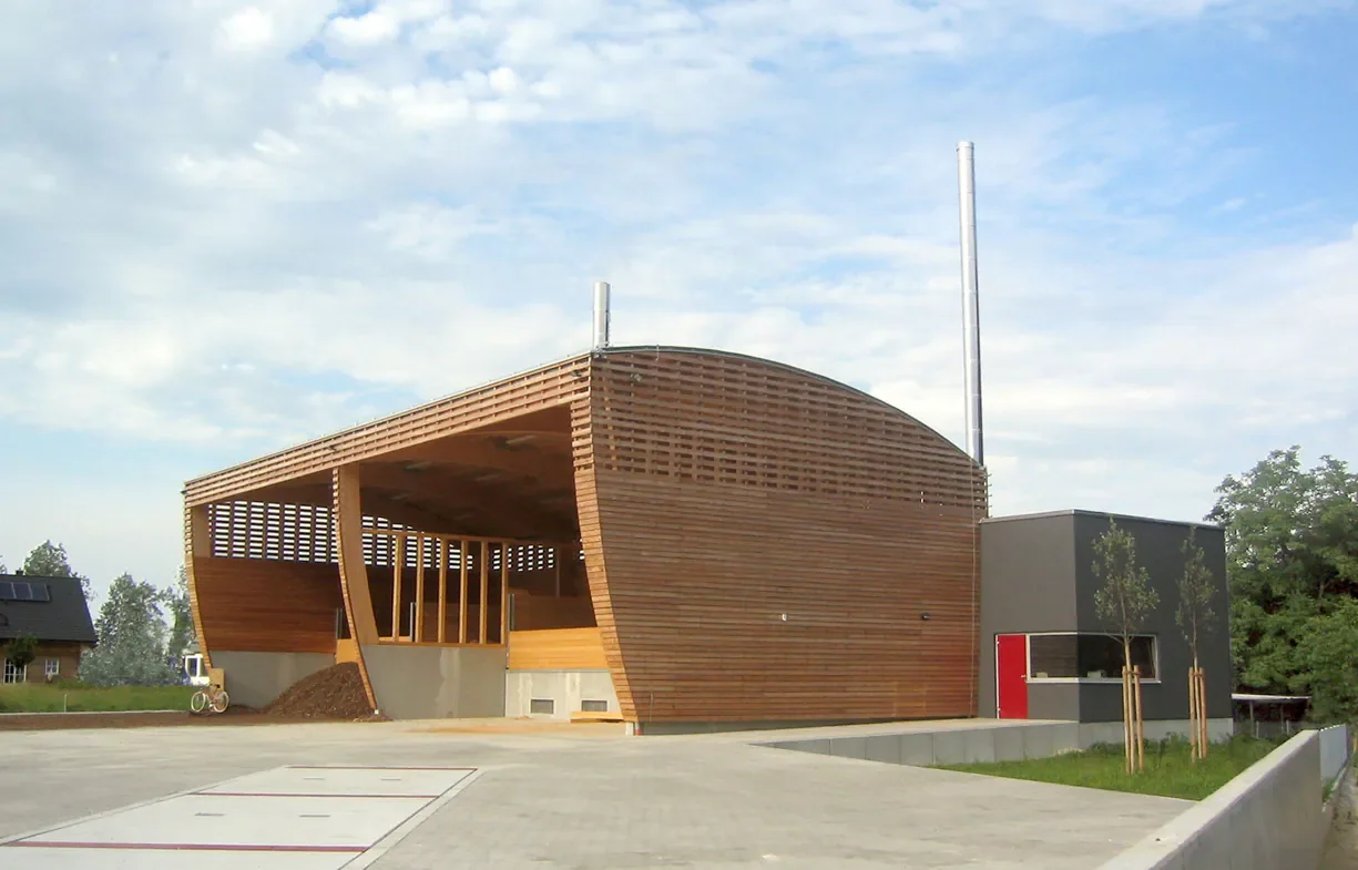 Modernes Gebäude mit Holzfassade und Doppel-Türme im Außenbereich, umgeben von Bäumen und einem gepflasterten Platz
