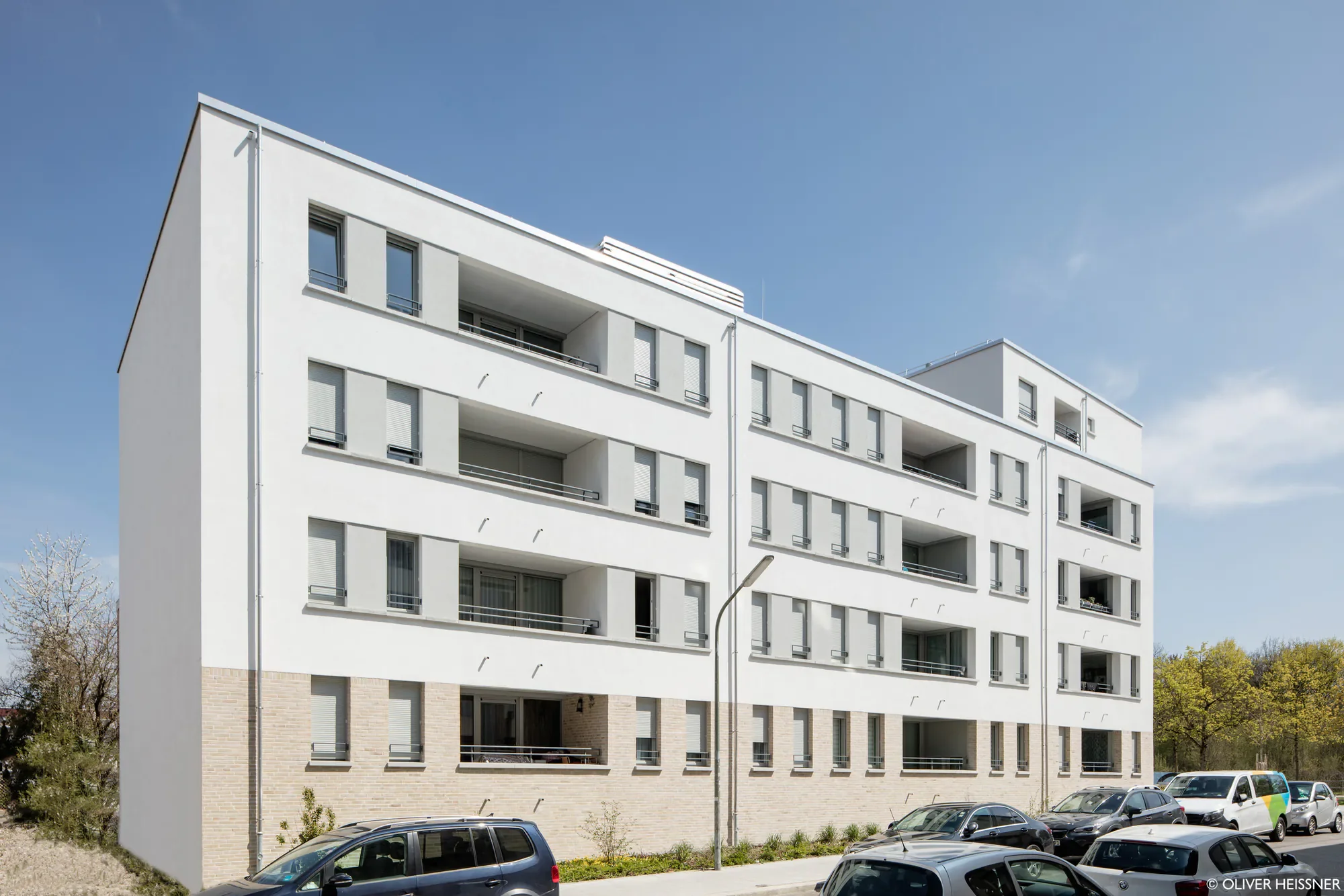 Modernes weißes Mehrfamilienhaus mit mehreren Balkonen und weißen Außenwänden gegen blauen Himmel.