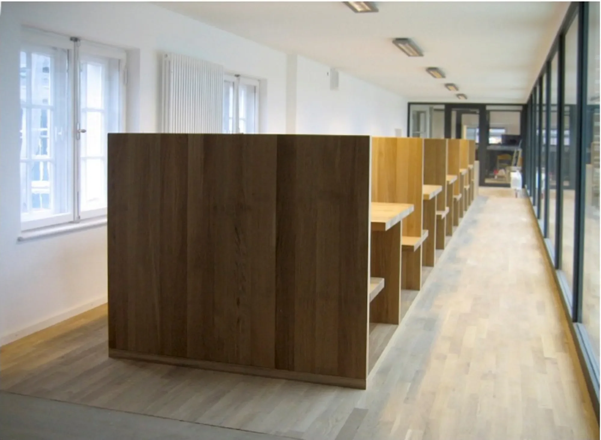 Bücherschrank in einem hellen, modernen Raum, mit großen Fenstern auf der linken Seite und Glastür auf der rechten Seite.