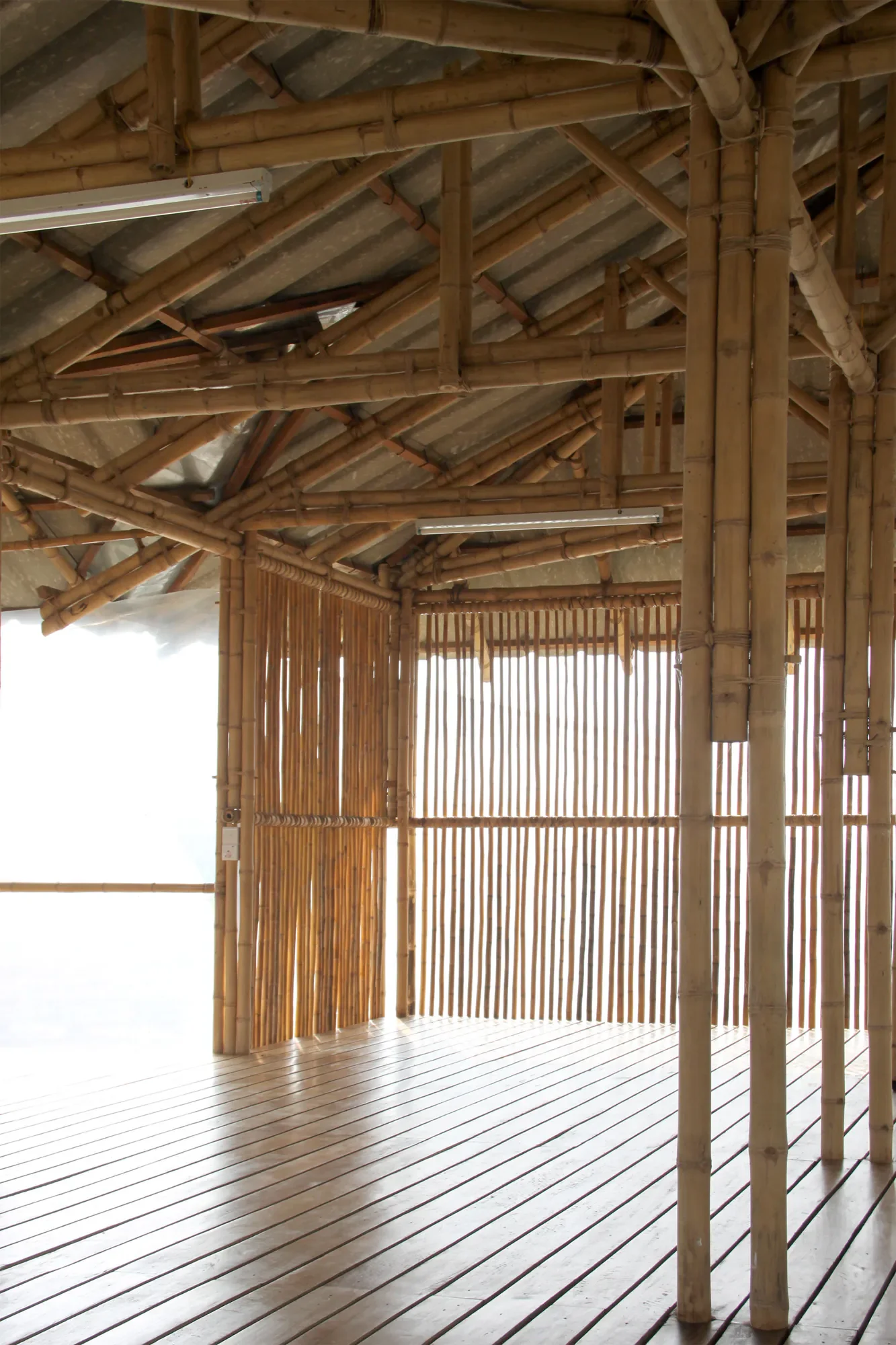 Innenansicht eines Gebäudes aus Bambus mit lamellartigem Wanddesign, Holzboden und sichtbarer Bambuskonstruktion an der Decke.