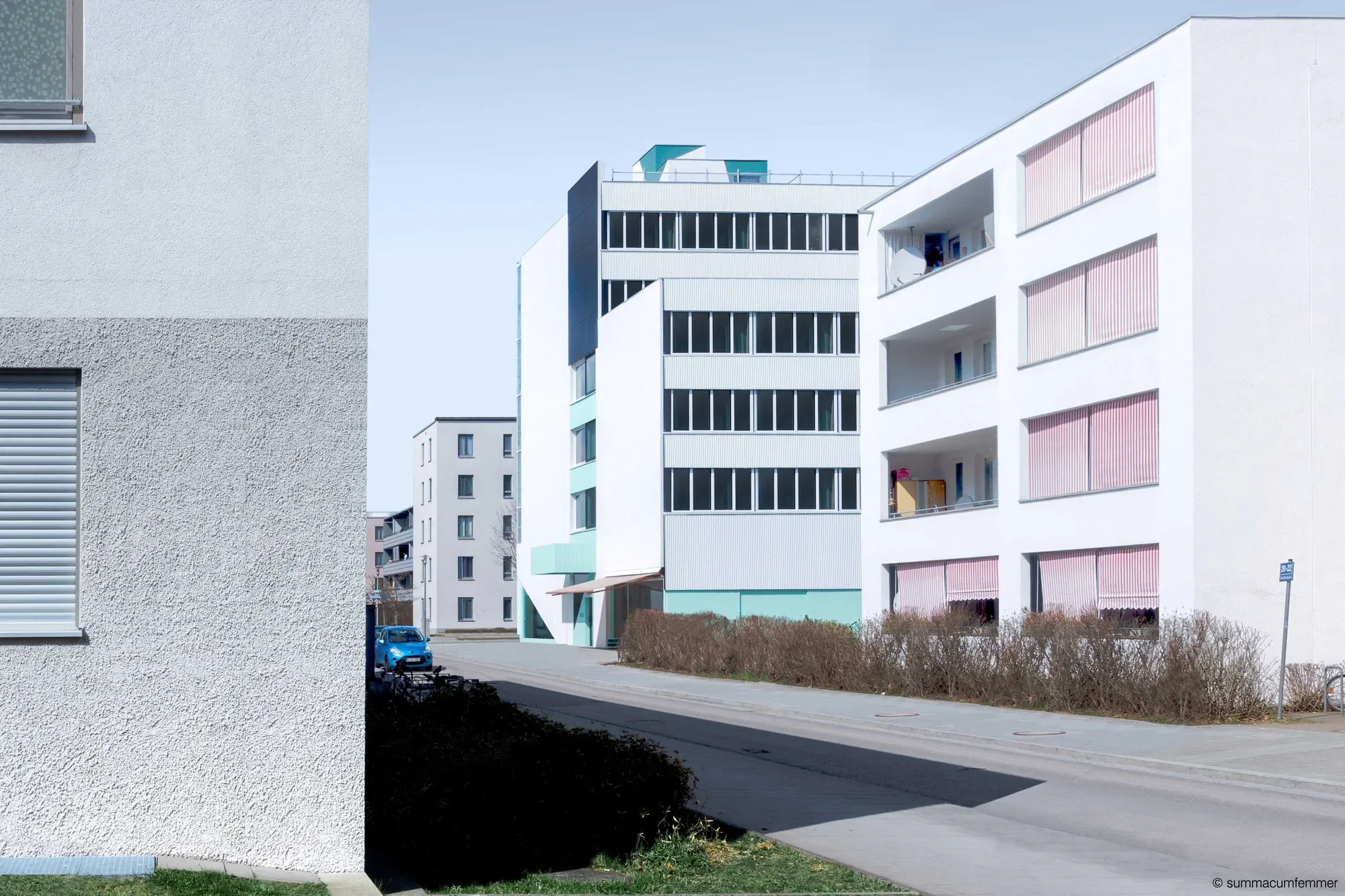 Moderne weiße Wohnanlage mit Balkonen und großen Fenstern, im Vordergrund ein schwarzer Schatten, blauer Himmel.