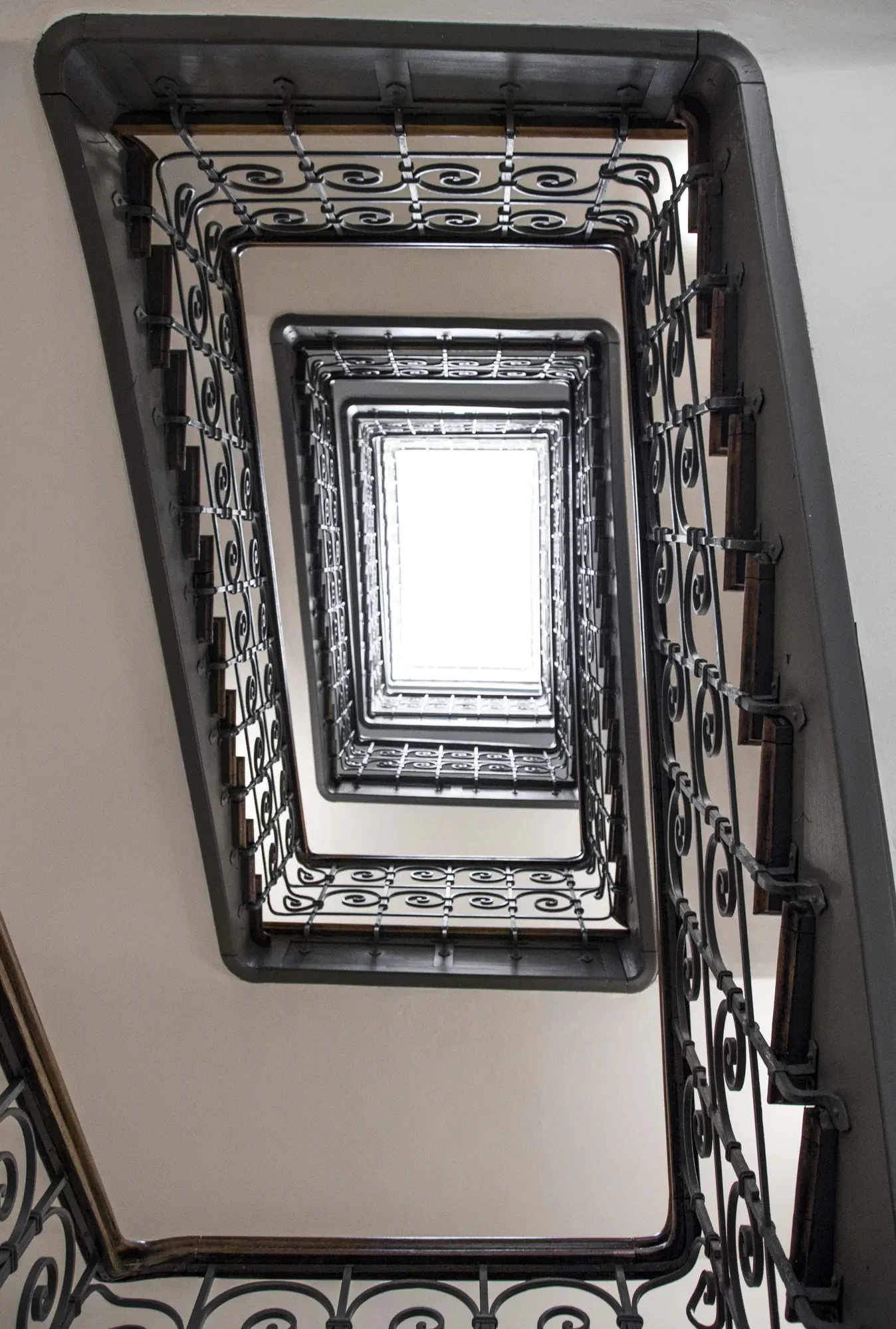 Blick nach oben auf ein spiralförmiges Treppenhaus mit schmiedeeisernen Geländern, das sich nach oben erstreckt.