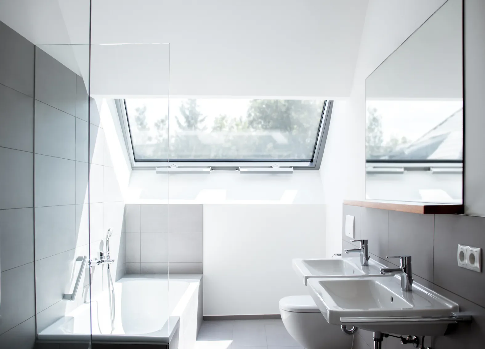 Ein modernes Badezimmer mit Doppelwaschbecken, WC, einer großen Dachfenster und Spiegel.