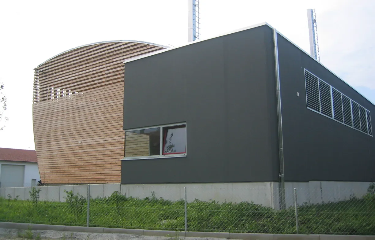 Moderne Gebäude mit dunklem Fassaden und Holzelementen, umgeben von einem grünen Garten und einem Zaun.