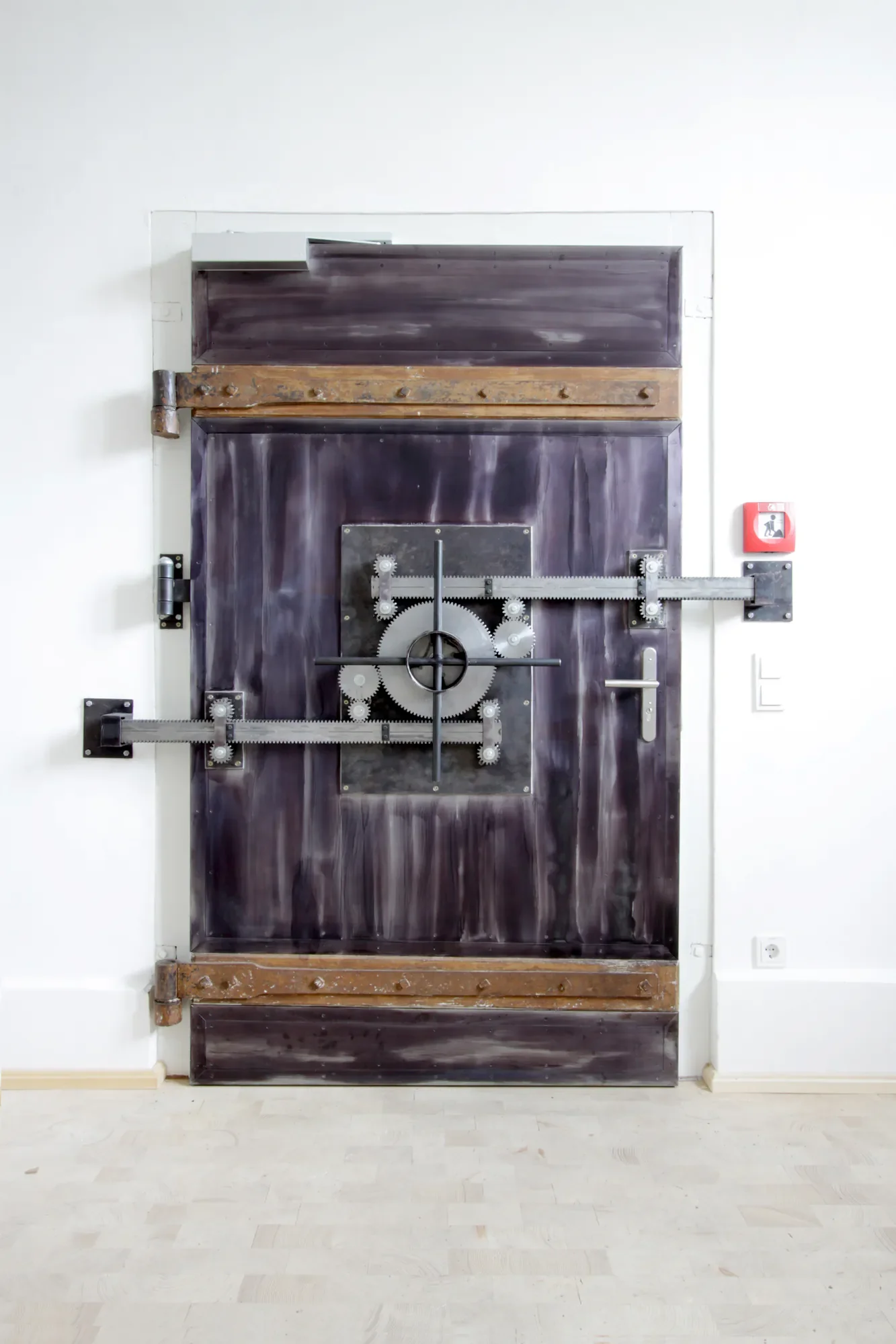 Eine Tür mit mechanischen Zahnrädern und Levellagern, vermutlich eine kunstvolle Tür oder ein Türersatz, an einer weißen Wand befestigt.