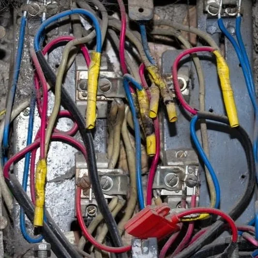 Frayed electrical power cord with exposed copper wiring resting on a flammable wooden floor surface.