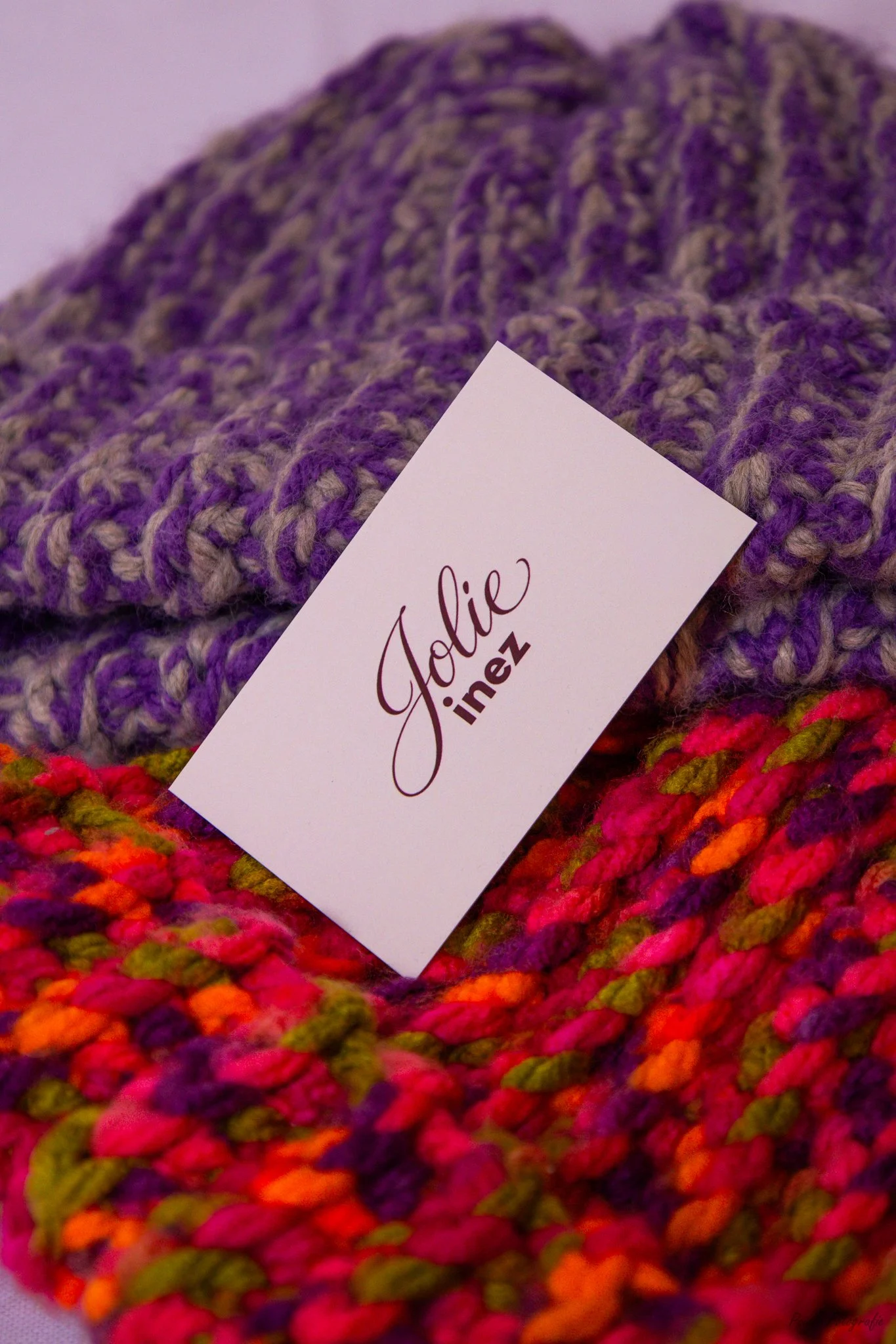 Close-up view of colorful, multicolored knitted yarn with a white label that reads "Jolie Janez".