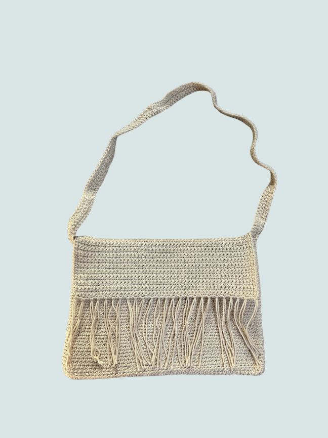 Cream-colored crochet handbag with fringes hanging from the bottom, against a light blue background.