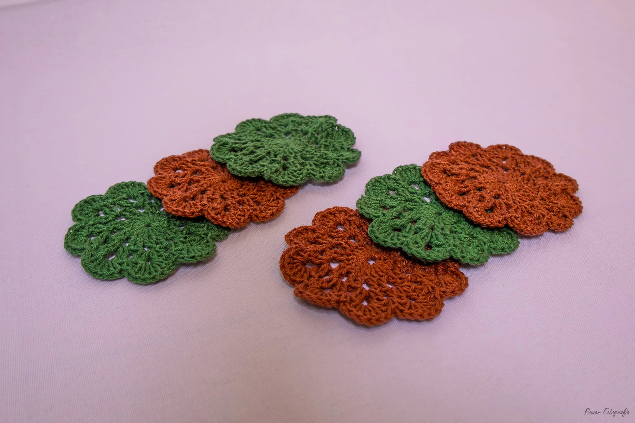 Colorful crocheted coasters in green and orange, scattered on a light pink surface.