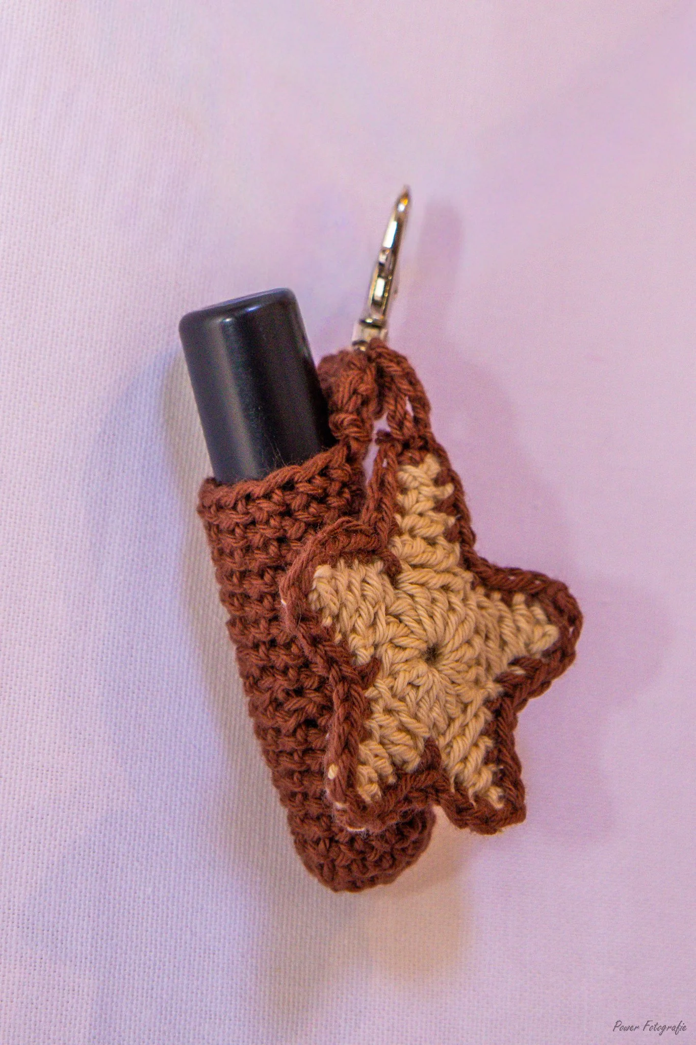 A crochet Christmas stocking with a black handle or object inside, hanging against a pink background.