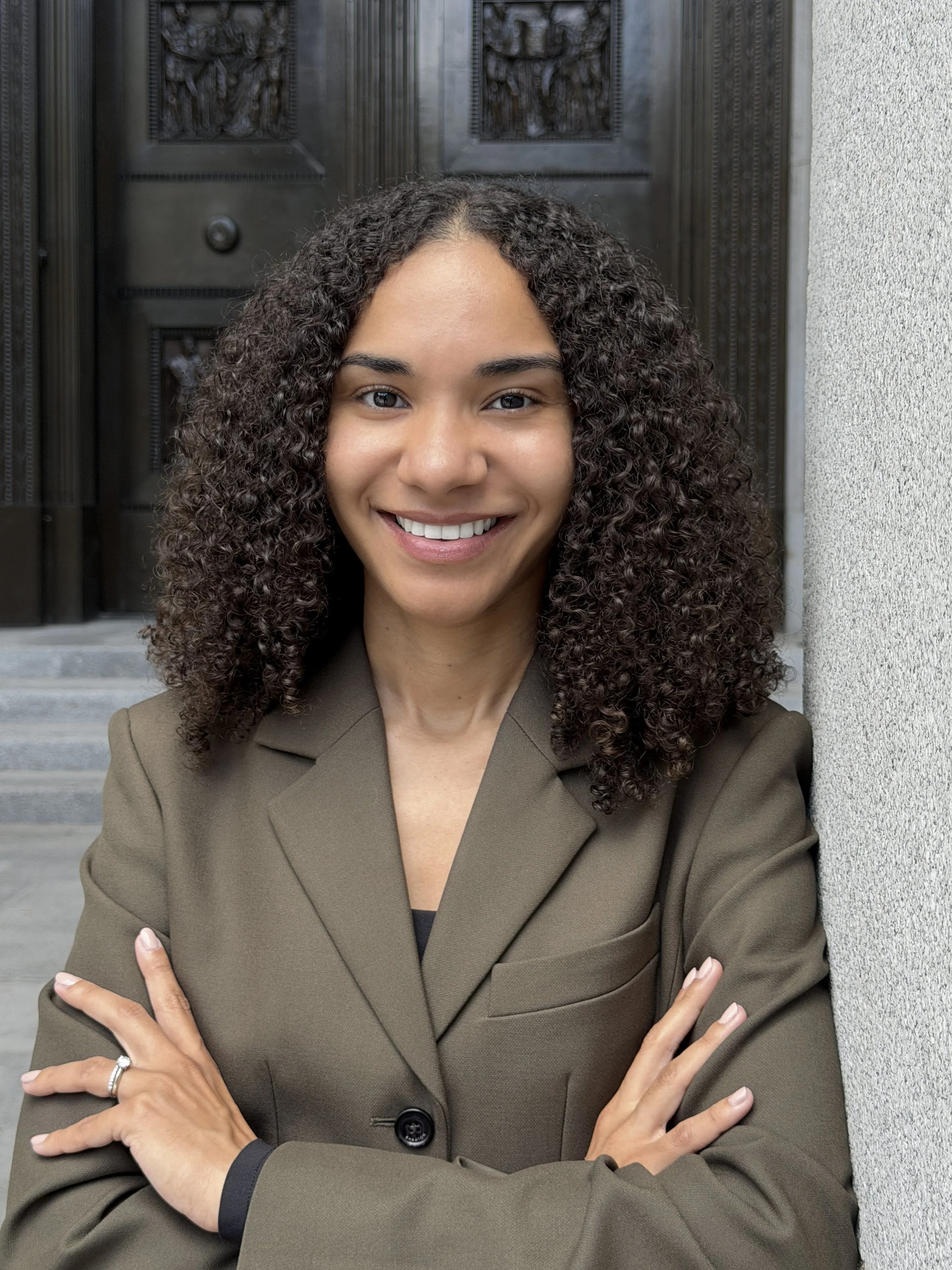 April Nutakor, immigration lawyer, smiling with her arms crossed beside the bronze doors of a courthouse