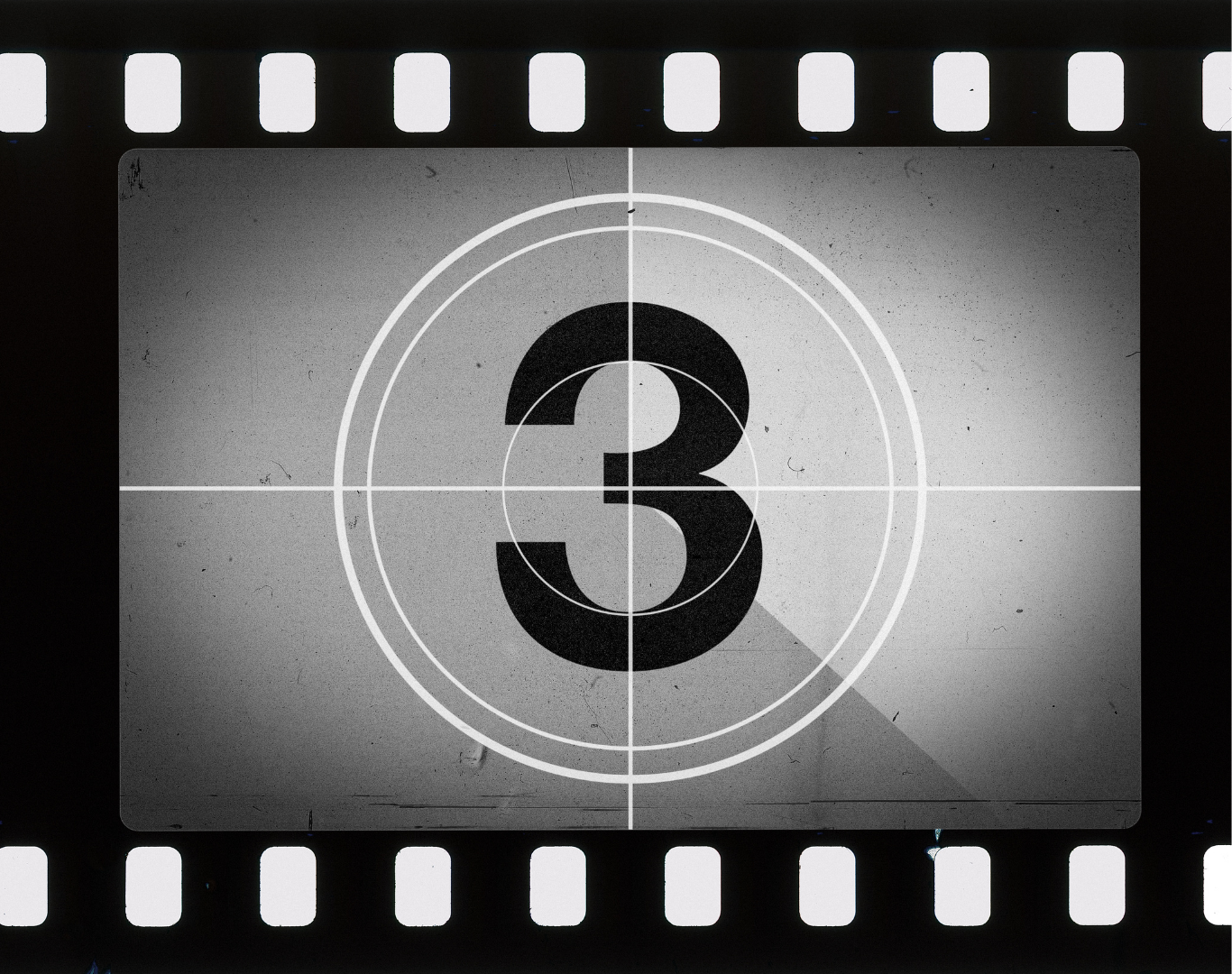 A black-and-white film countdown timer displaying the number three, with a gray background and film perforations along the top and bottom edges.