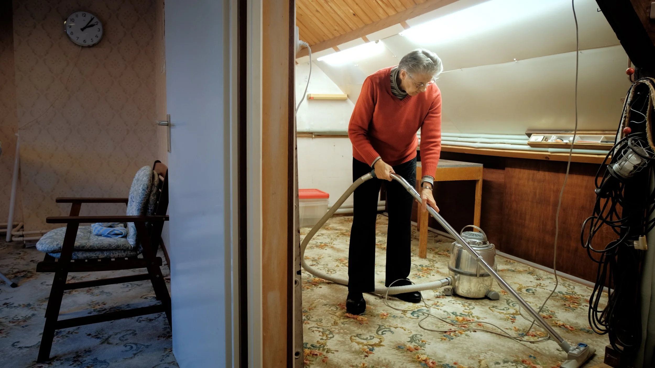 Een oudere vrouw stofzuigt een kamer met een tapijt.